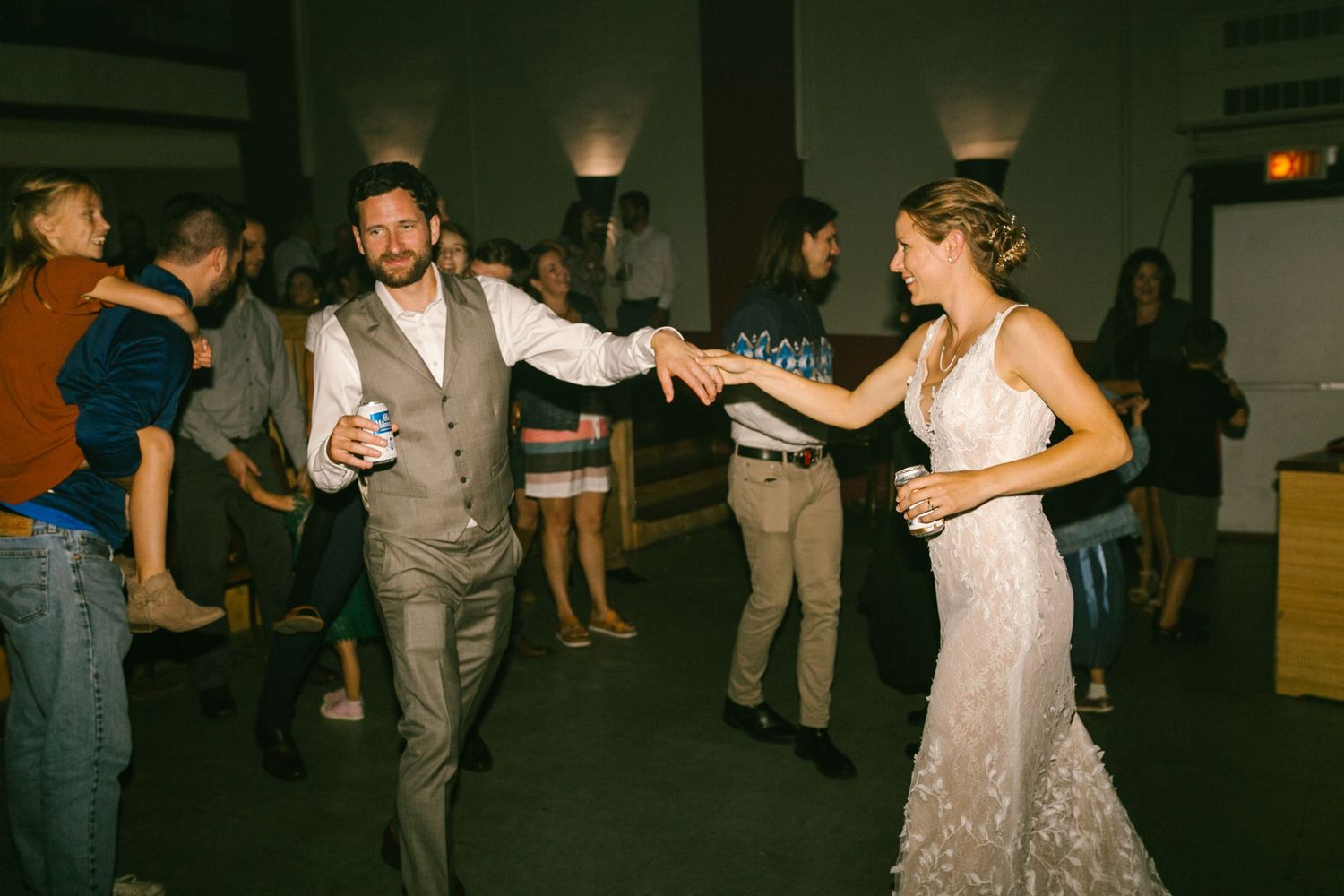 A couple dances joyfully at their wedding reception while other guests mingle in the background.