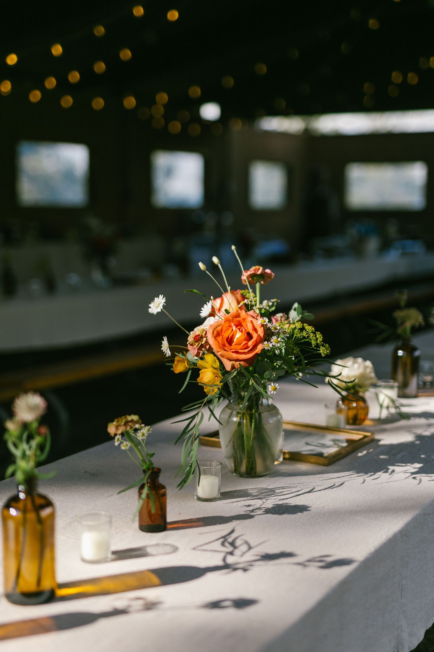Wedding reception table decorated with fresh floral centerpieces and amber bottles.