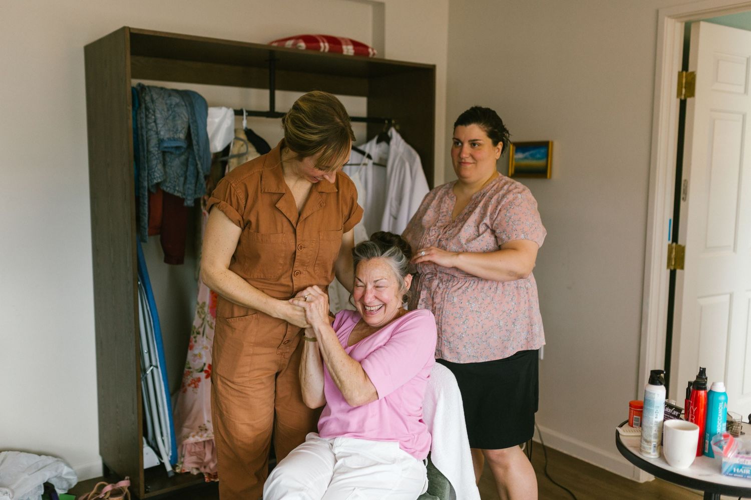 Three people share a lighthearted moment together in a casual home setting with a closet visible in the background.