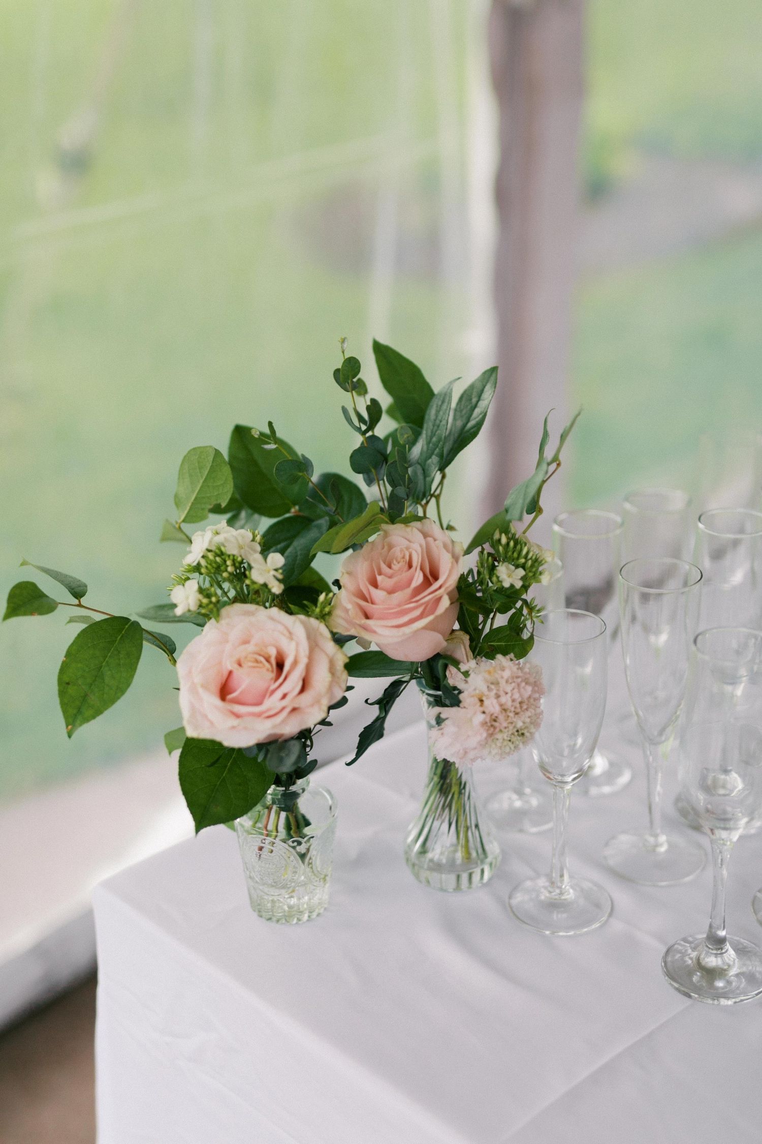 Elegant table setting with pink roses and greenery in small glass vases on white linens at a formal event.