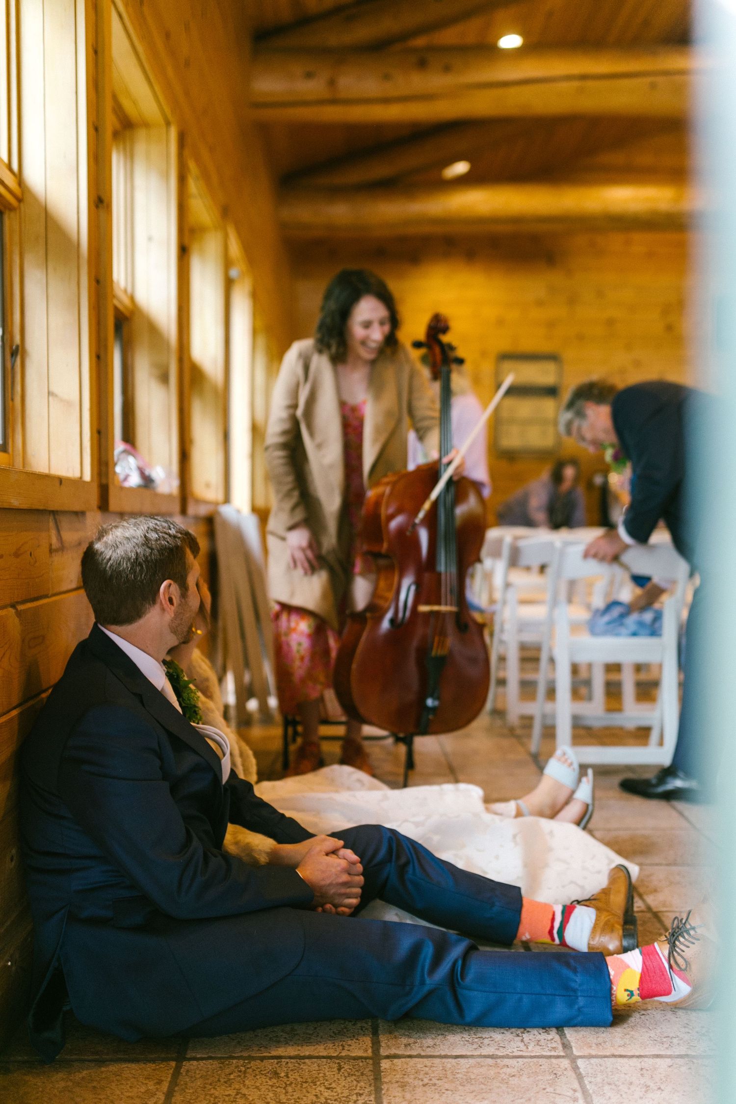 Musicians setting up instruments in a warm wooden hallway with sunlight streaming through windows.