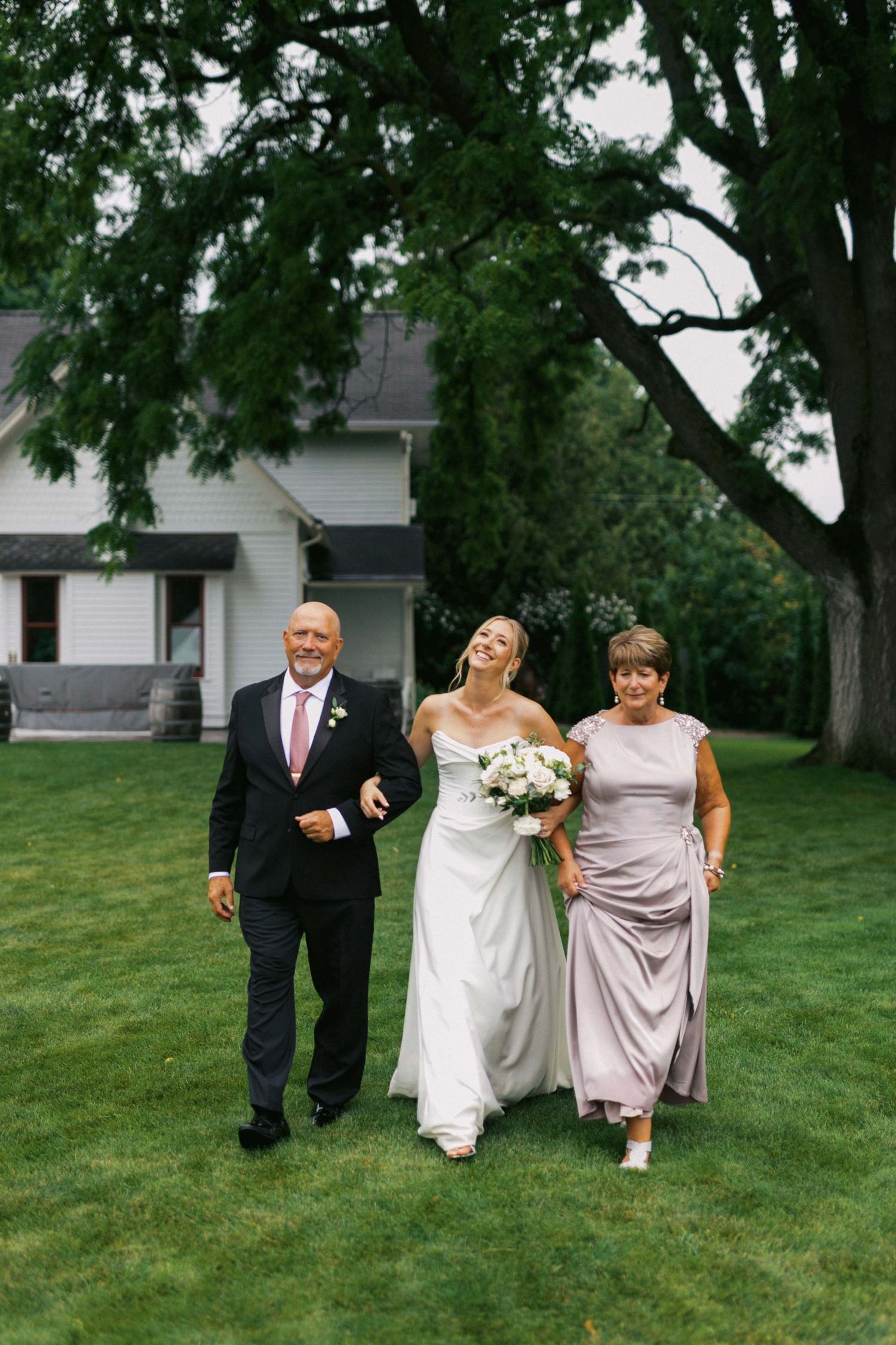 A bride's parents guide her to her outdoor ceremony at Aurora Cellars in Traverse City, Michigan.