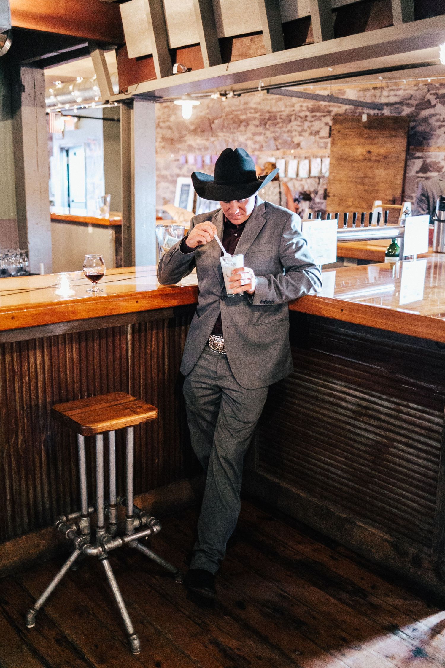 Person in a dark suit and hat inspects a wooden bench seating area in a rustic restaurant interior.