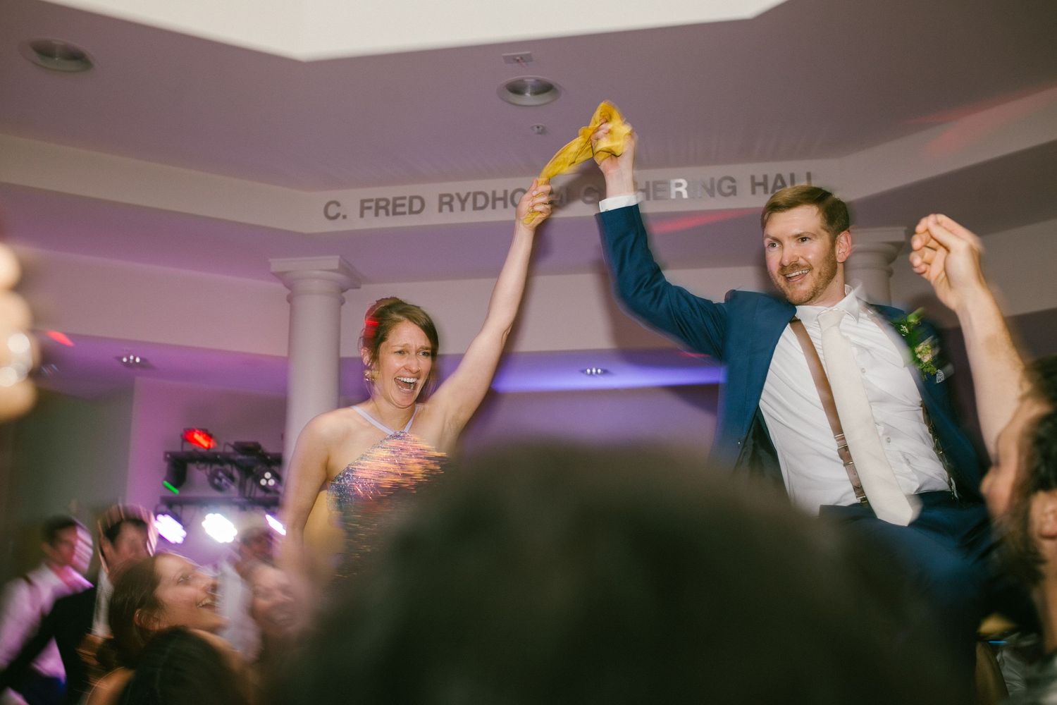 A couple dances joyfully at a reception venue with raised hands while celebrating on the dance floor.