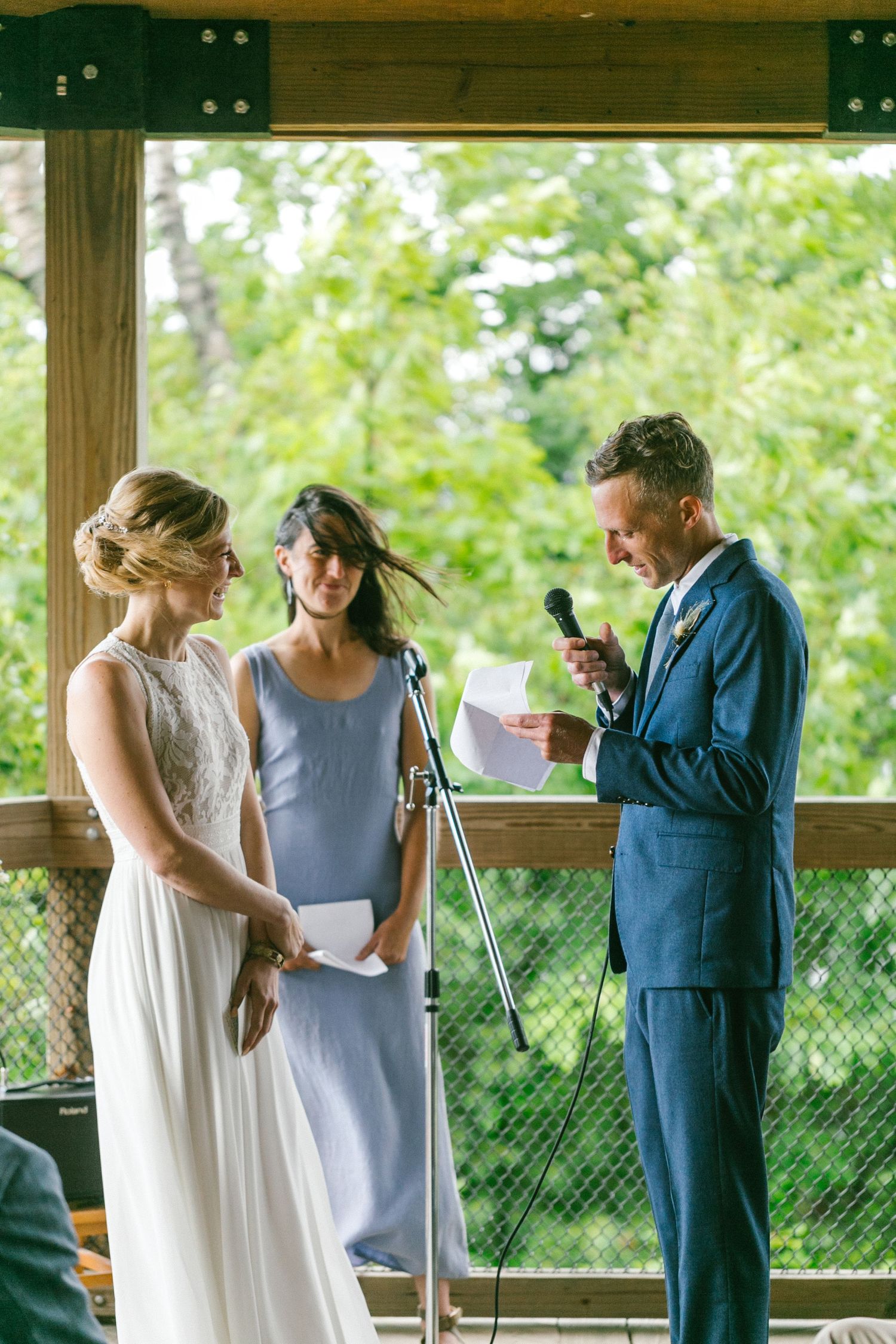 Wedding ceremony participants exchanging vows in an outdoor pavilion surrounded by greenery.