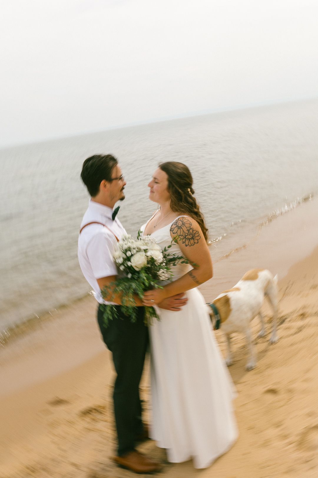 A couple shares a romantic moment on a sandy beach with white flowers and formal attire.