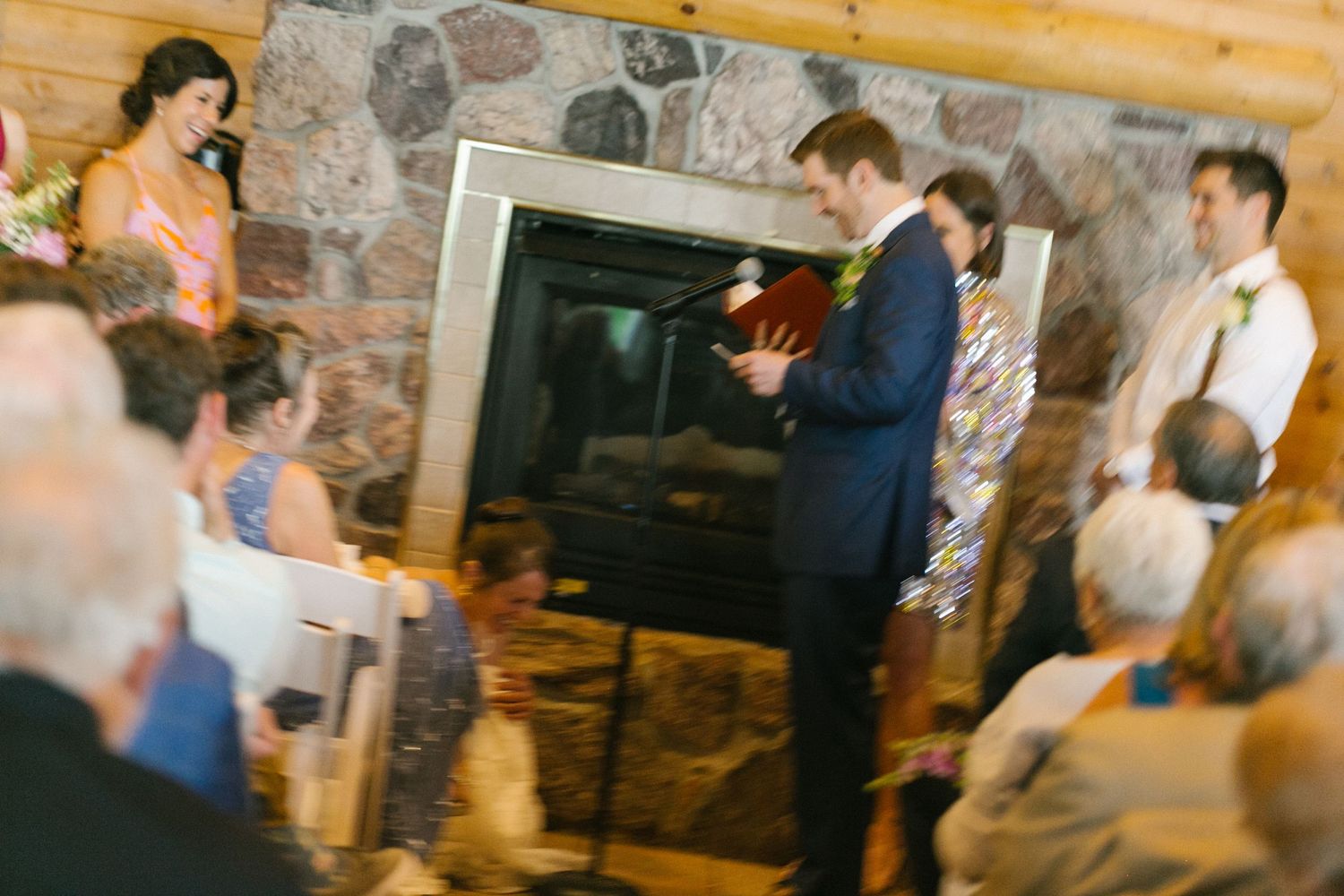 A group gathers around a fireplace in what appears to be a cozy cabin setting during a social gathering.