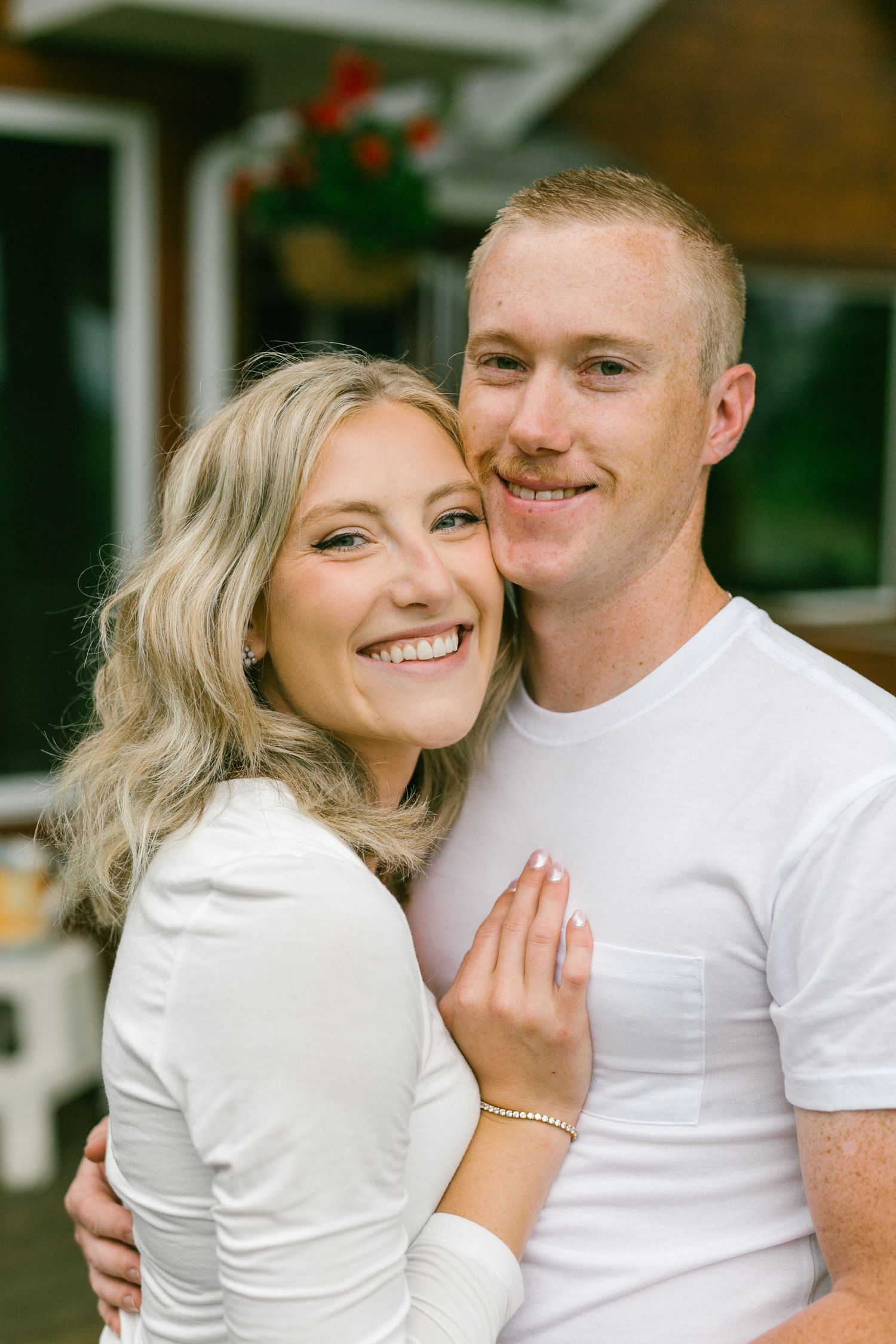 A happy couple embraces and smiles while standing outside their home with a hanging Christmas decoration.
