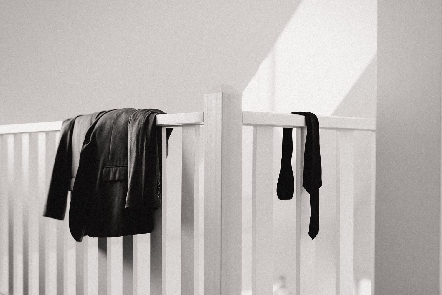 Black clothing items hang over white railing in a minimalist black and white composition.