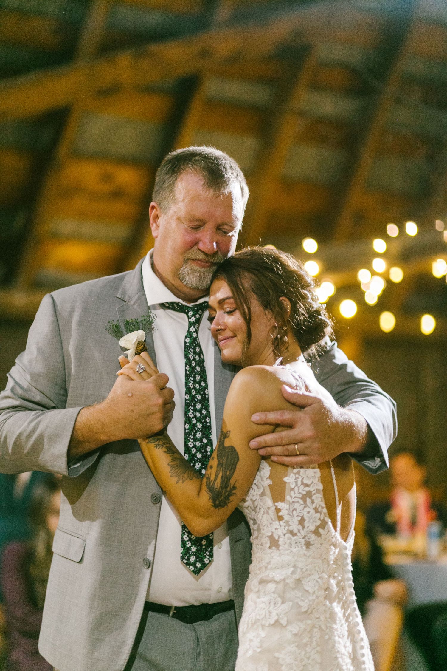 A tender father and daughter dance moment under twinkling lights at a rustic barn wedding reception.