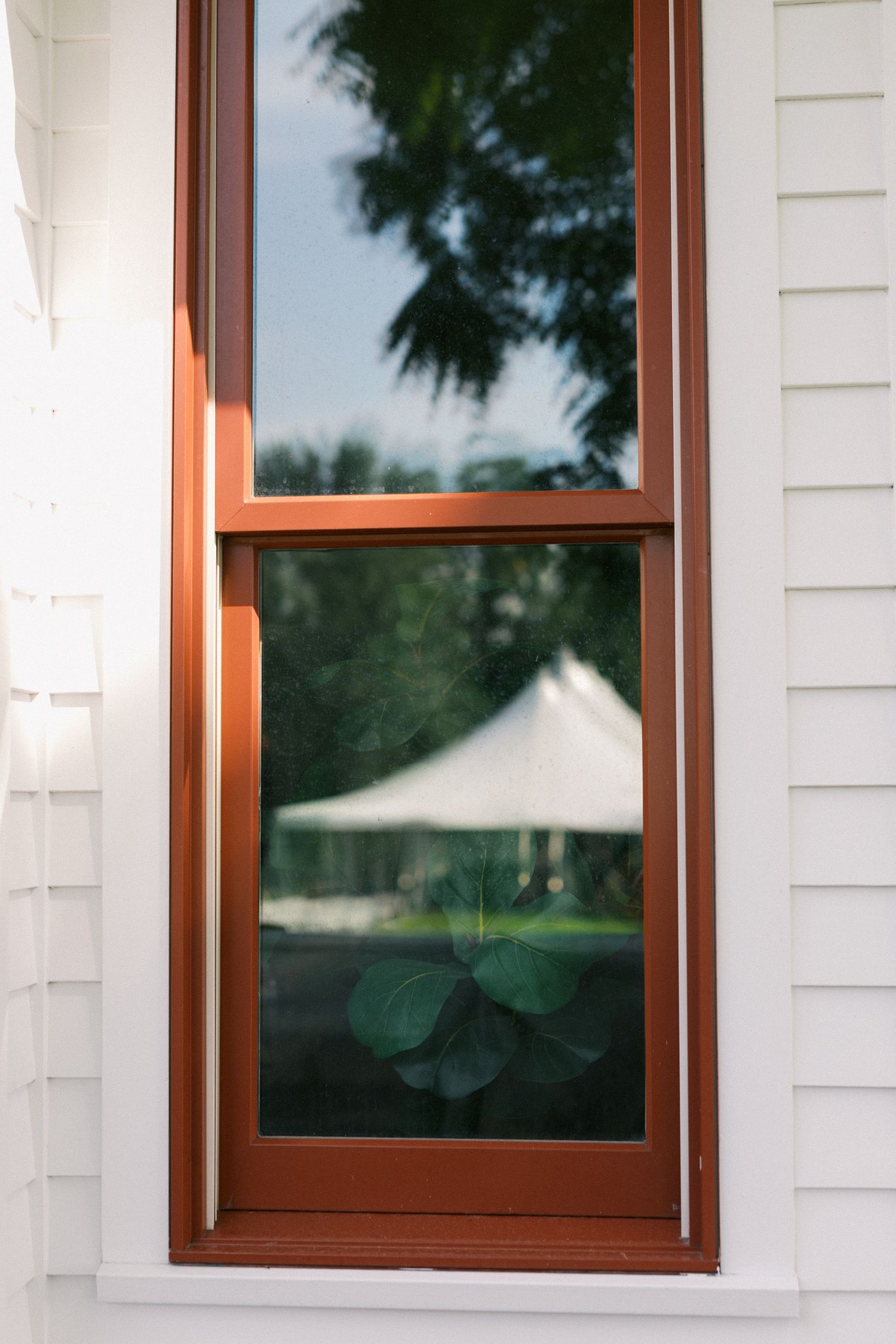 Three copper-framed windows with white trim are mounted on a white siding exterior wall of a building.