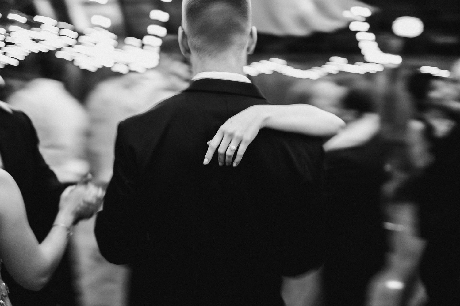 Black and white photo of a couple dancing at a wedding reception, woman's hand with ring on man's back.