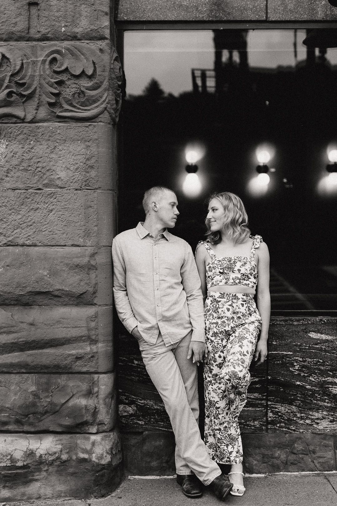 Black and white photo of couple leaning against ornate stone building at night.