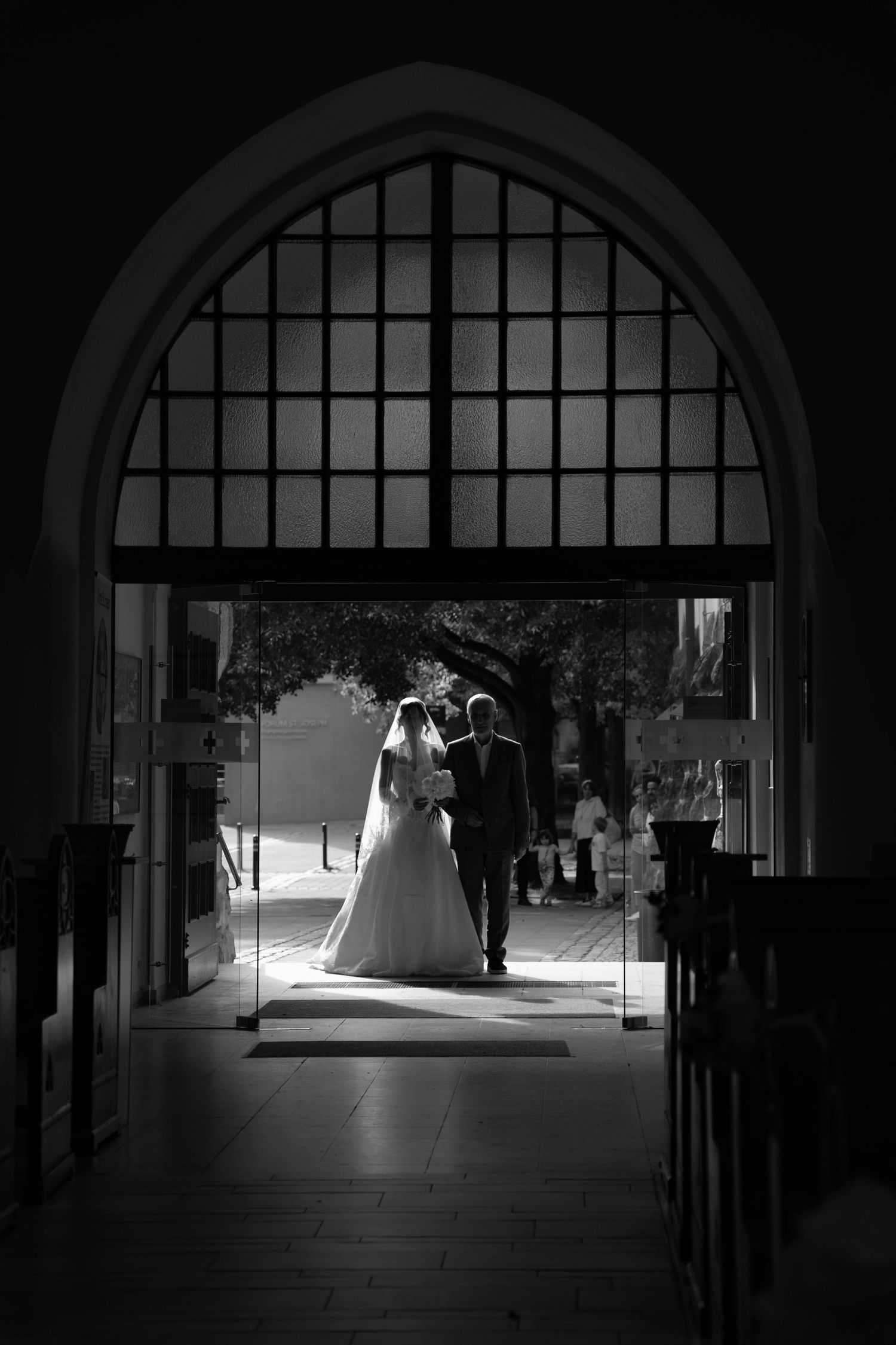 Black and white photo of bride and groom silhouetted in arched church doorway on their wedding day.