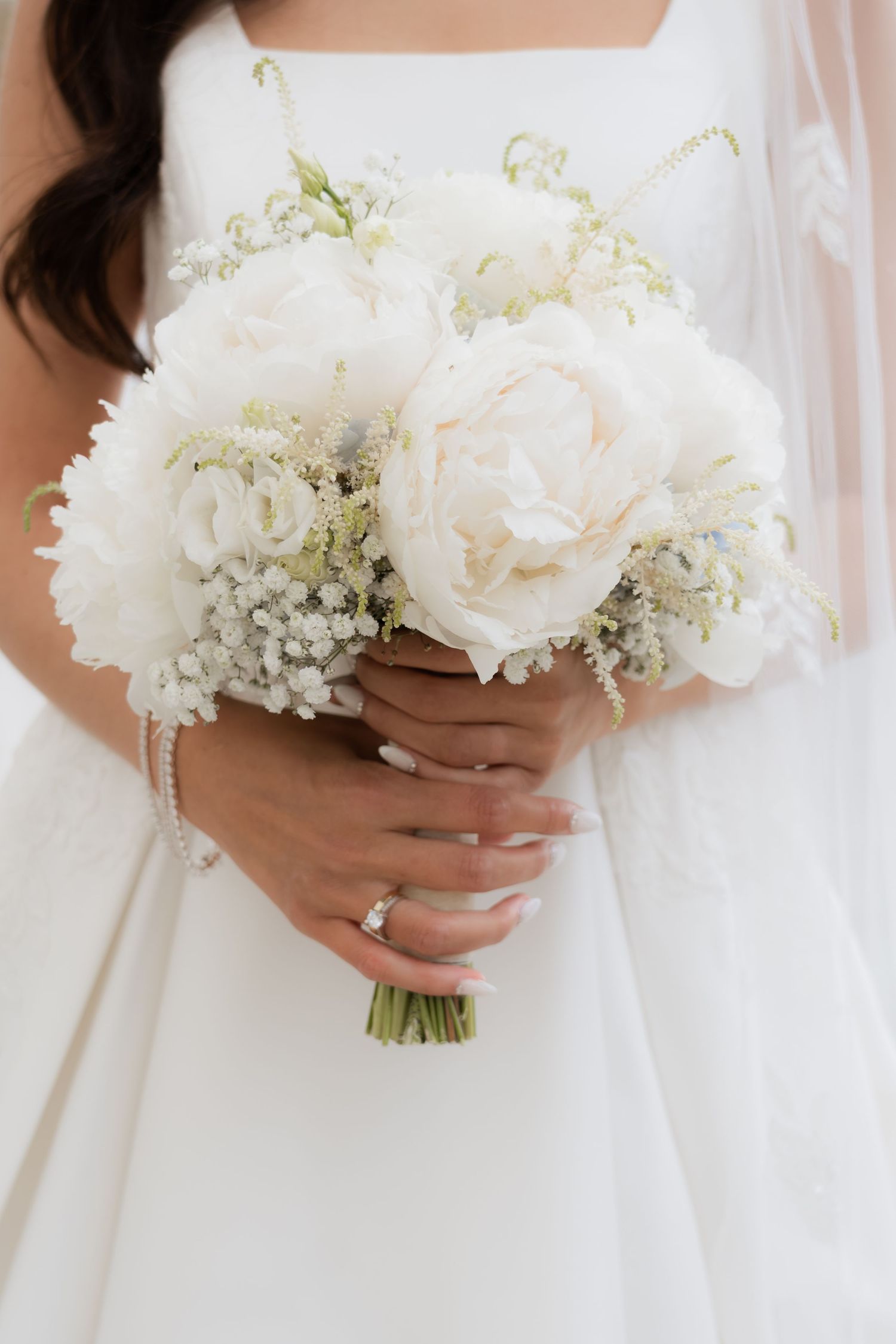 Bride holding white peony and baby's breath bouquet with diamond engagement ring.