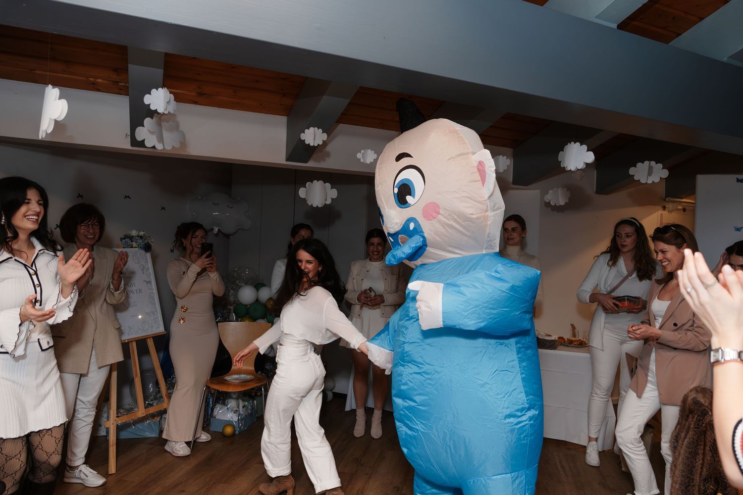 People dancing with a blue baby costume at a festive indoor baby shower party.