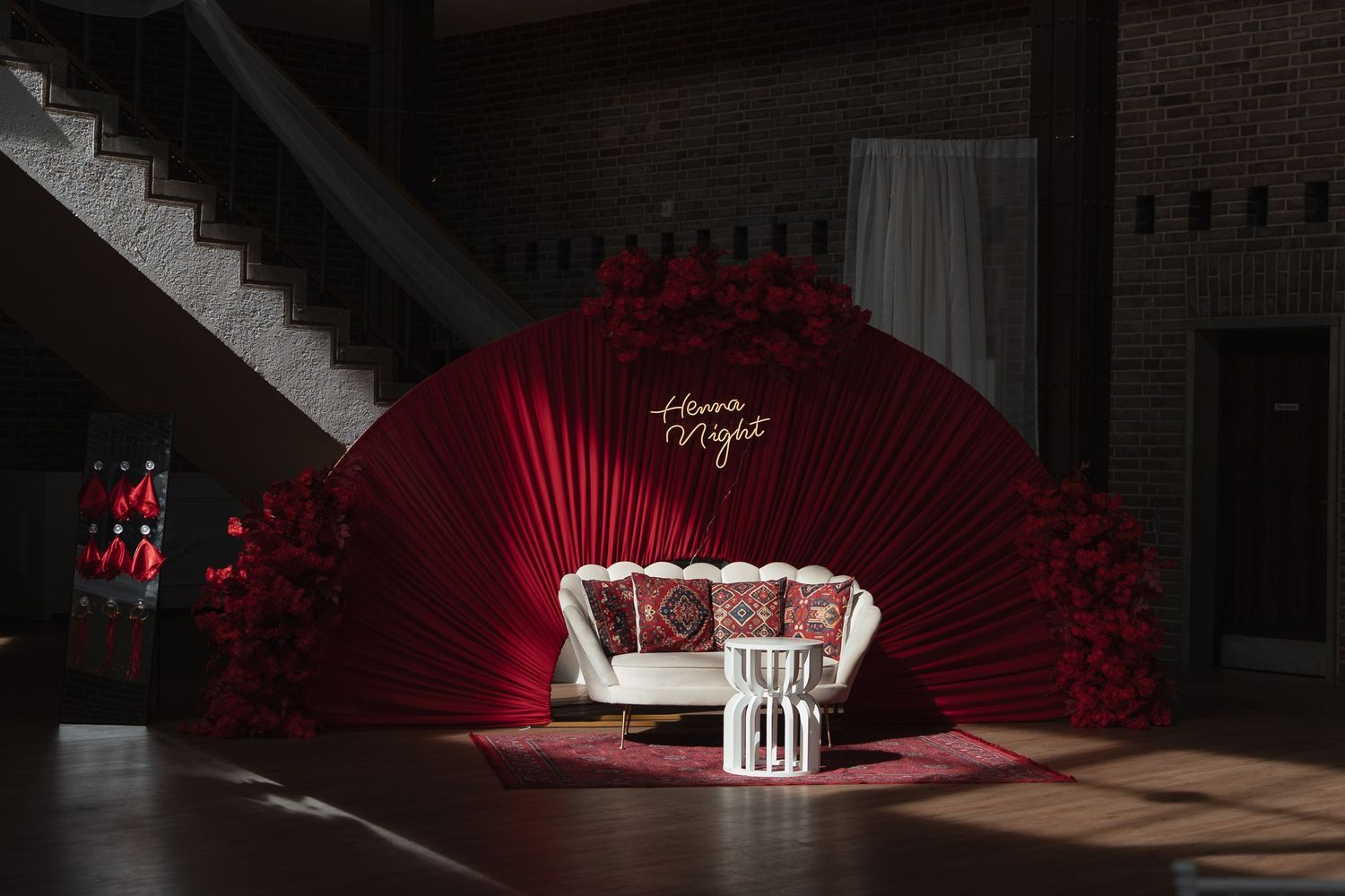 Dramatic red floral fan backdrop with white sofa for Henna Night wedding celebration setup.
