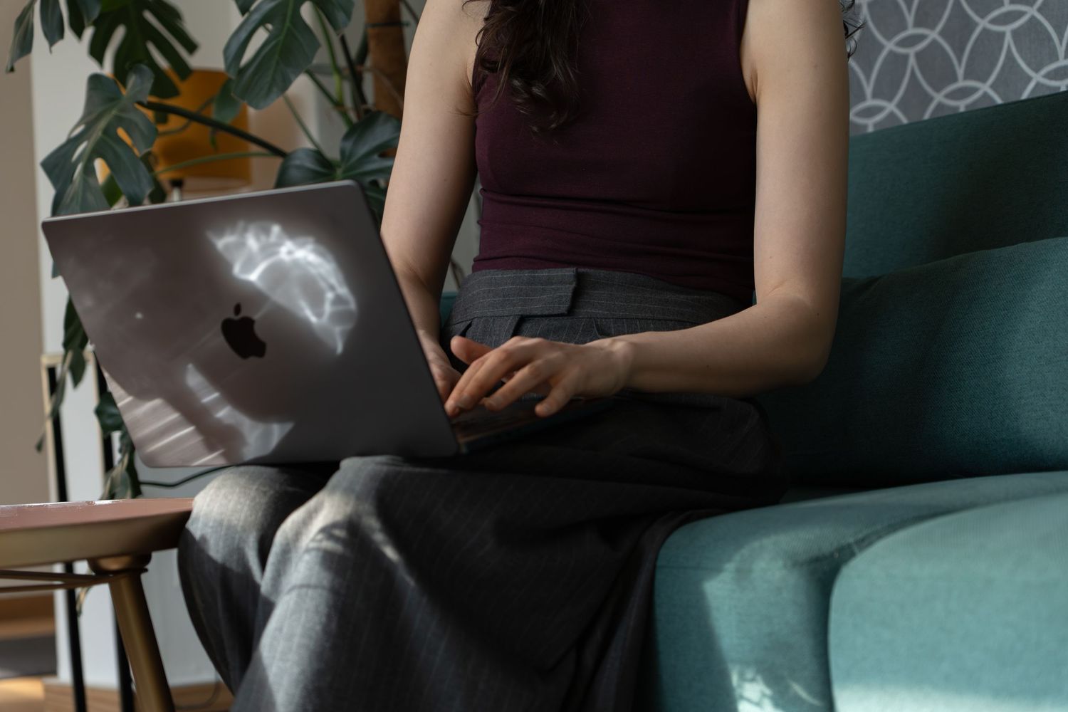 Woman sitting on a teal sofa using an Apple MacBook laptop in a cozy modern living room.