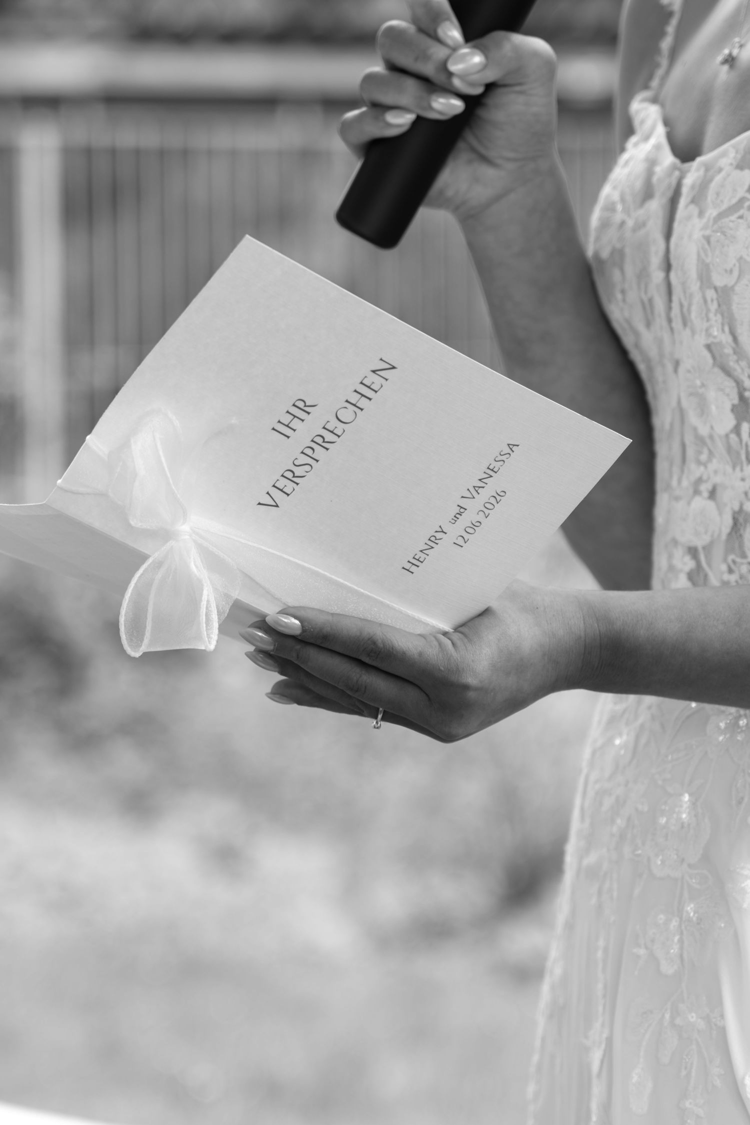 Bride holding wedding vow booklet titled her Vows during outdoor ceremony in lace gown.