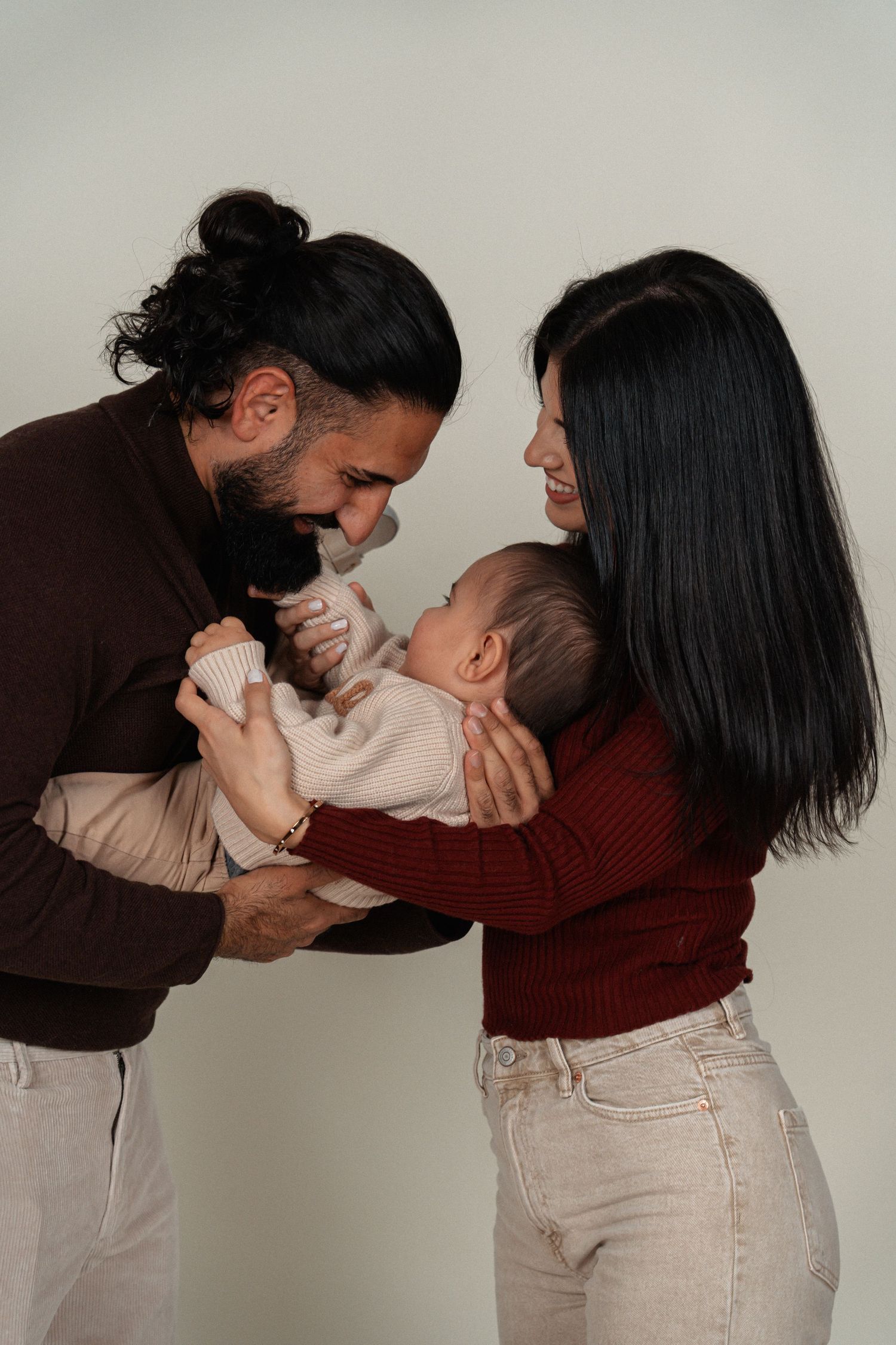 Smiling couple in casual attire lovingly holding their newborn baby.