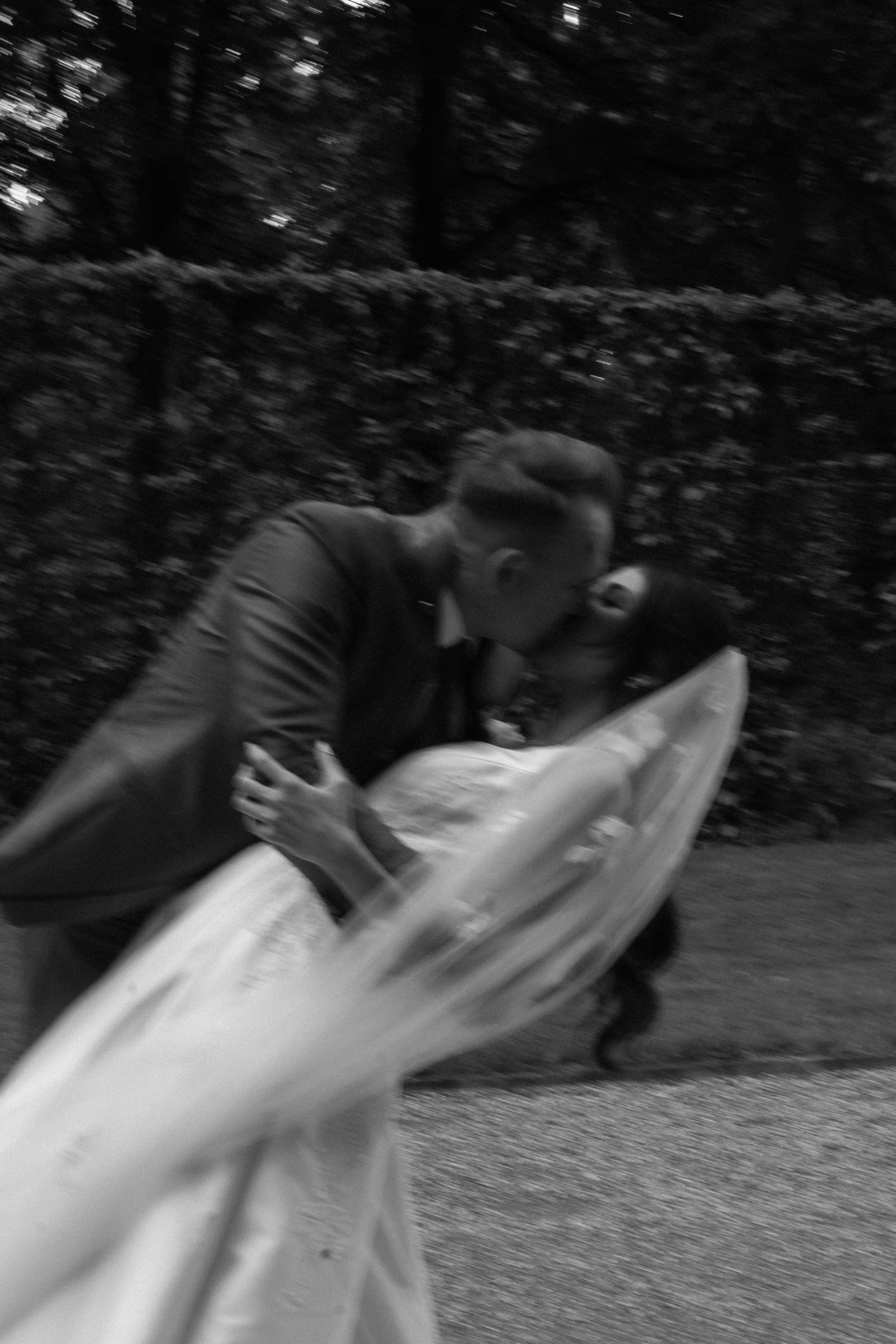 Black and white blurred motion photo of bride and groom sharing a romantic dip kiss outdoors.