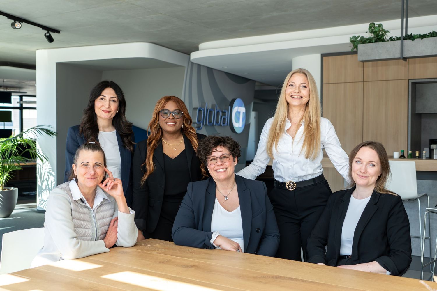 Professional team of six women smiling together in a modern office.