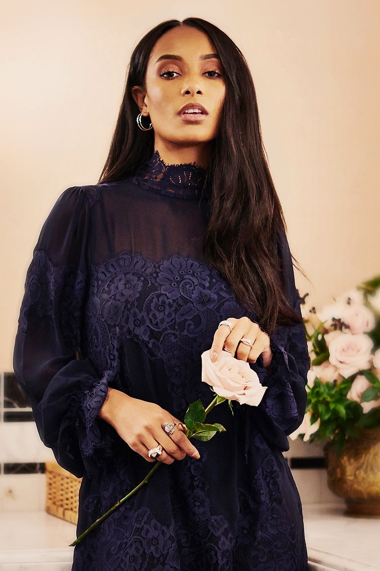 Woman in navy blue lace high-neck dress holding a white rose.