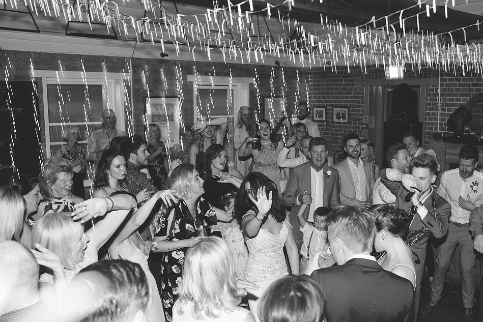 Black and white photo of wedding guests celebrating on a packed dance floor with streamers above.