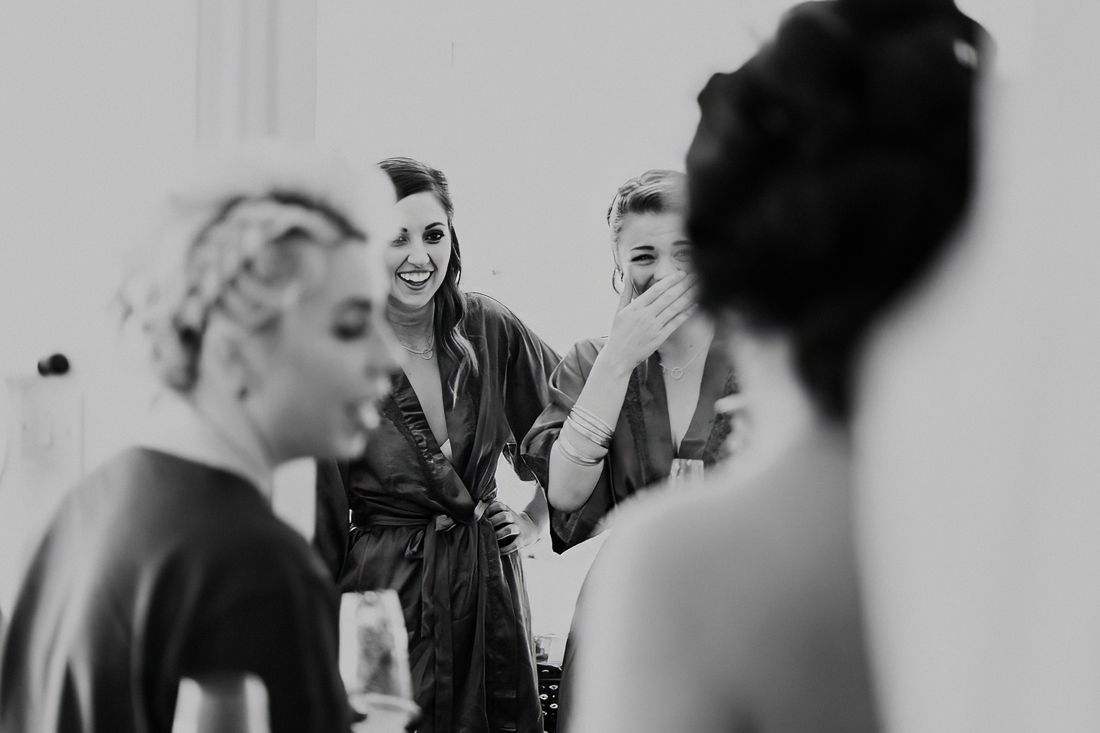 Bridesmaids laughing together in robes during wedding preparations in black and white.