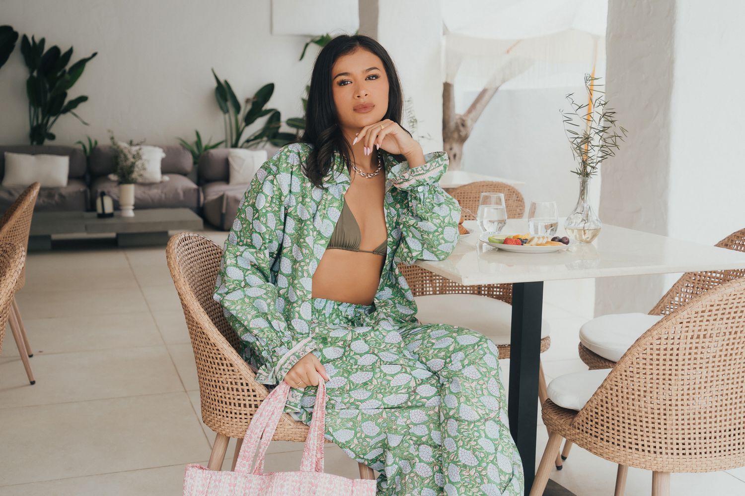 Woman in green floral co-ord set seated at outdoor patio table.