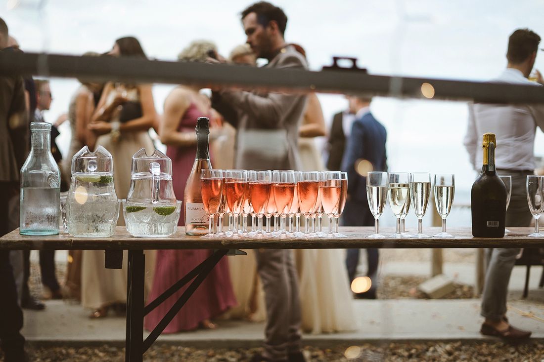 Wedding reception drinks table with rose champagne punch bowl and glasses outdoors.