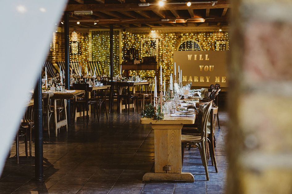 Rustic wedding venue decorated with fairy lights and will you marry me sign.