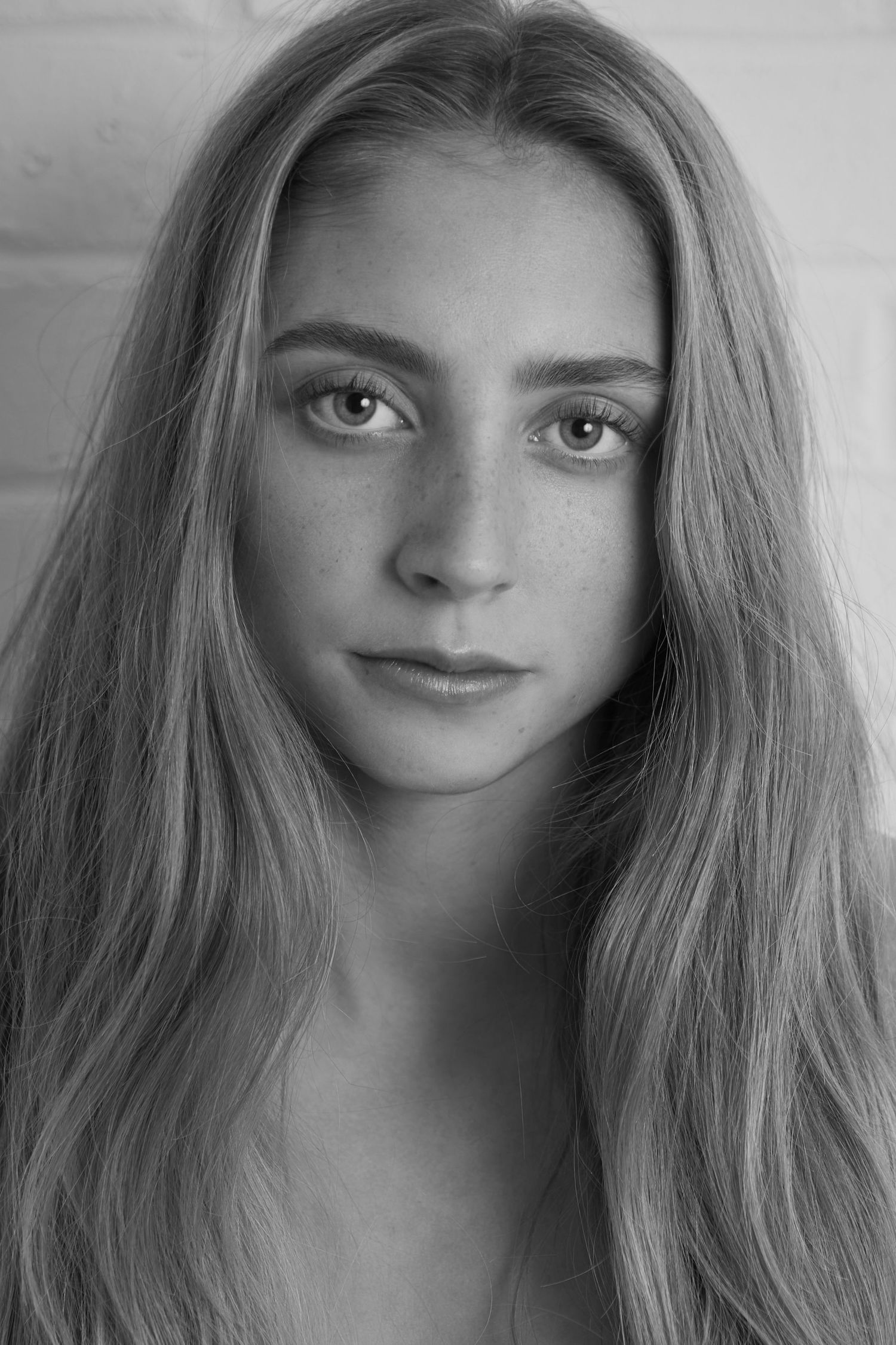 Black and white portrait of a young woman with long blonde hair and freckles looking directly at camera.