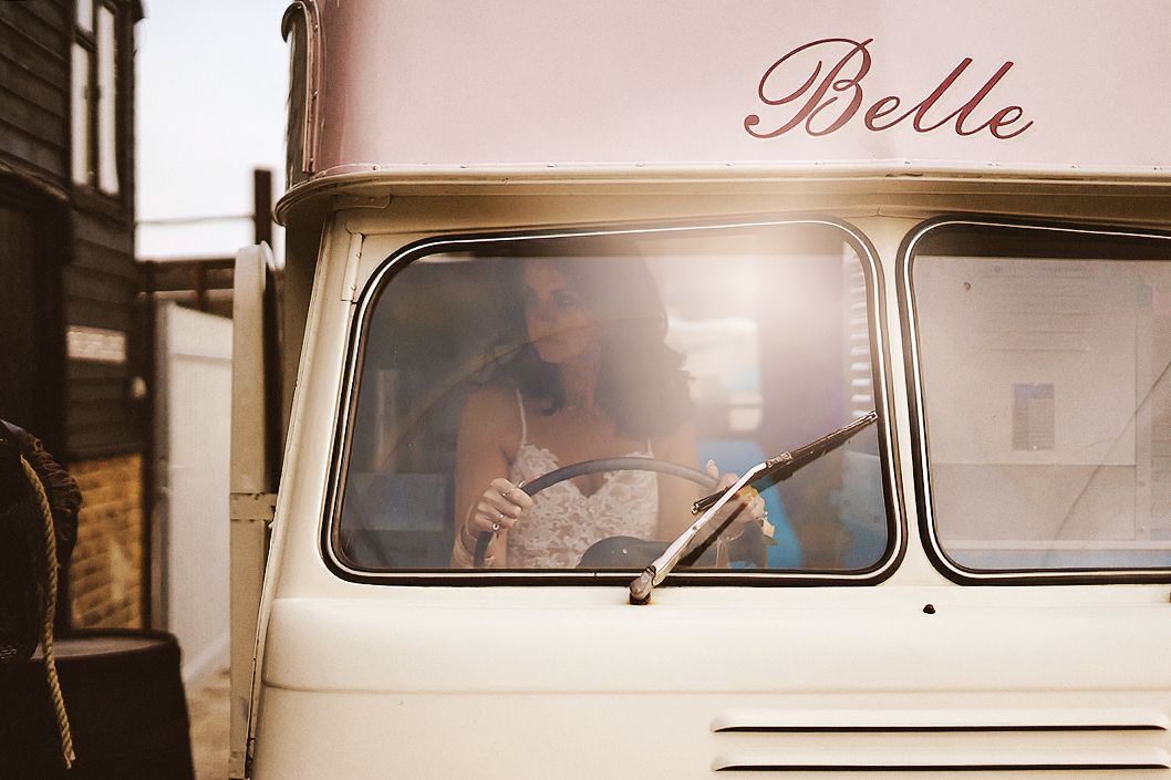 Woman sitting inside a vintage cream-colored van named Belle, bathed in warm sunlight.