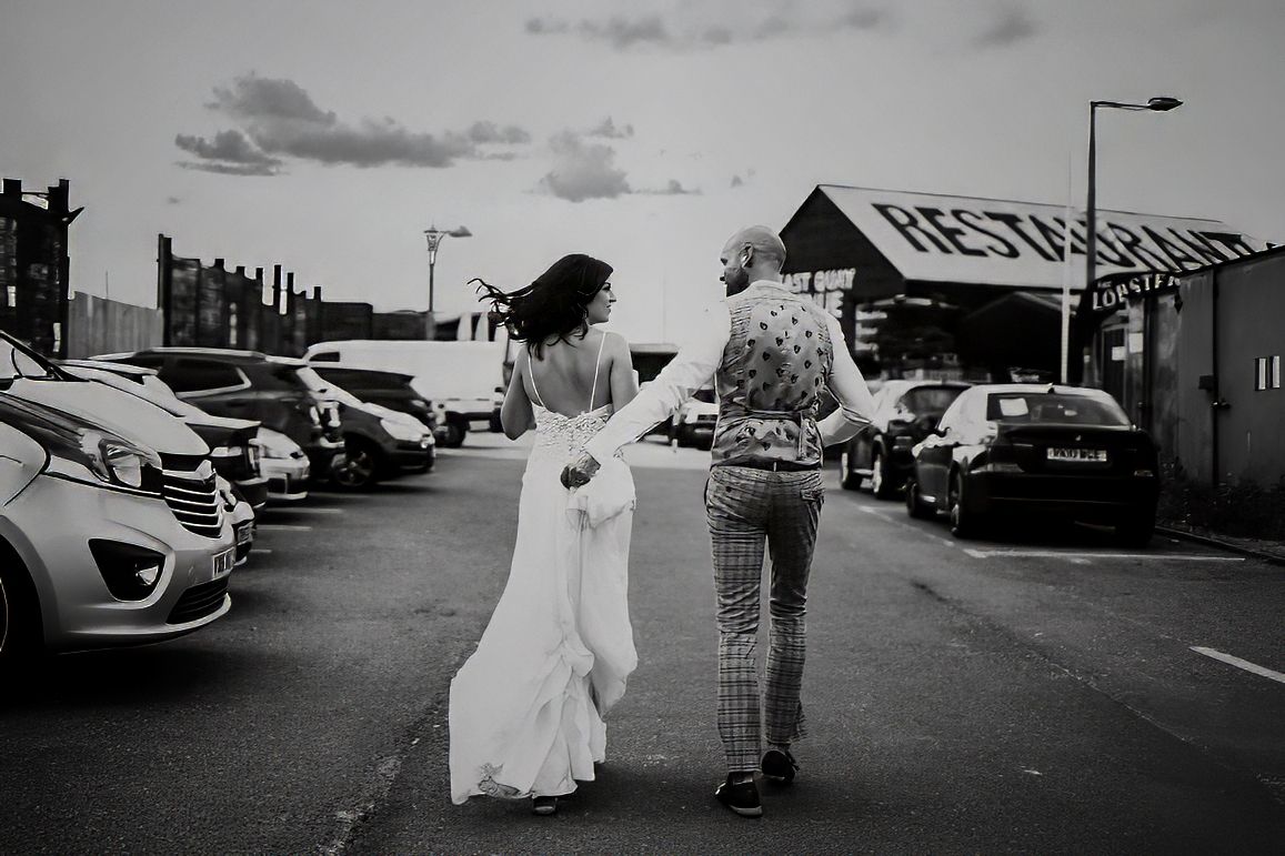 Bride and groom walking through car park in black and white wedding photo.