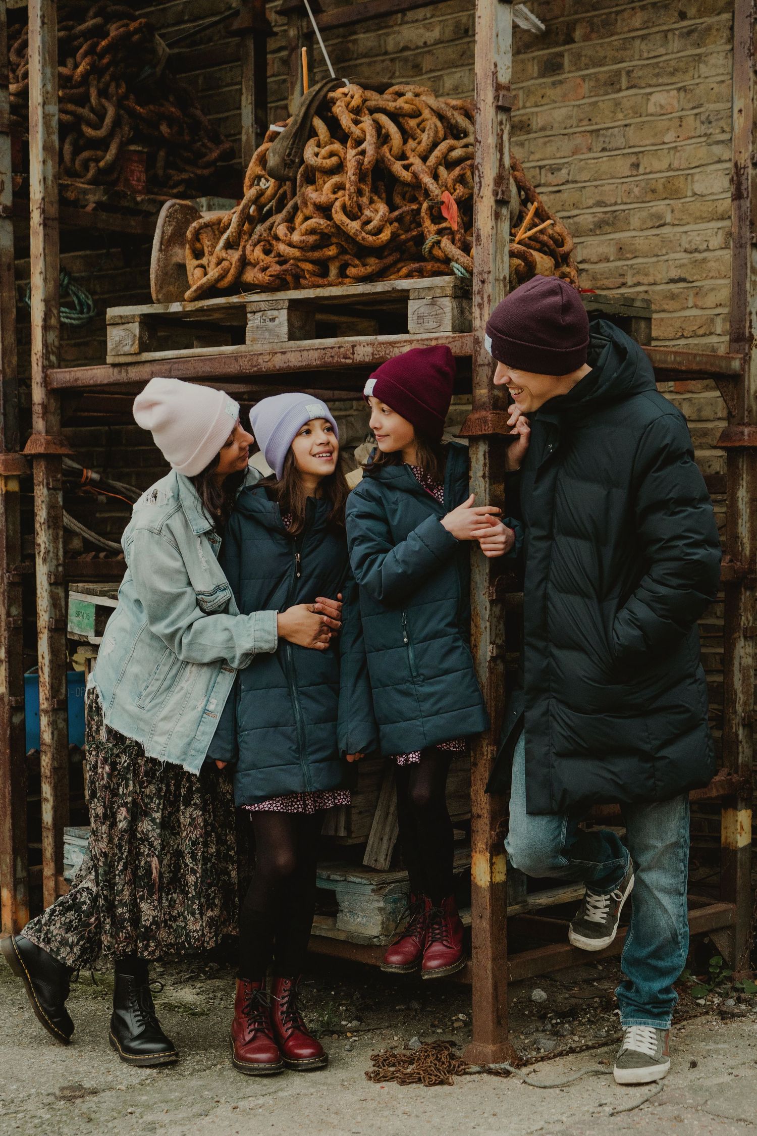 Family of four in winter coats and beanies gathered around rusty metal scaffolding in an urban setting.