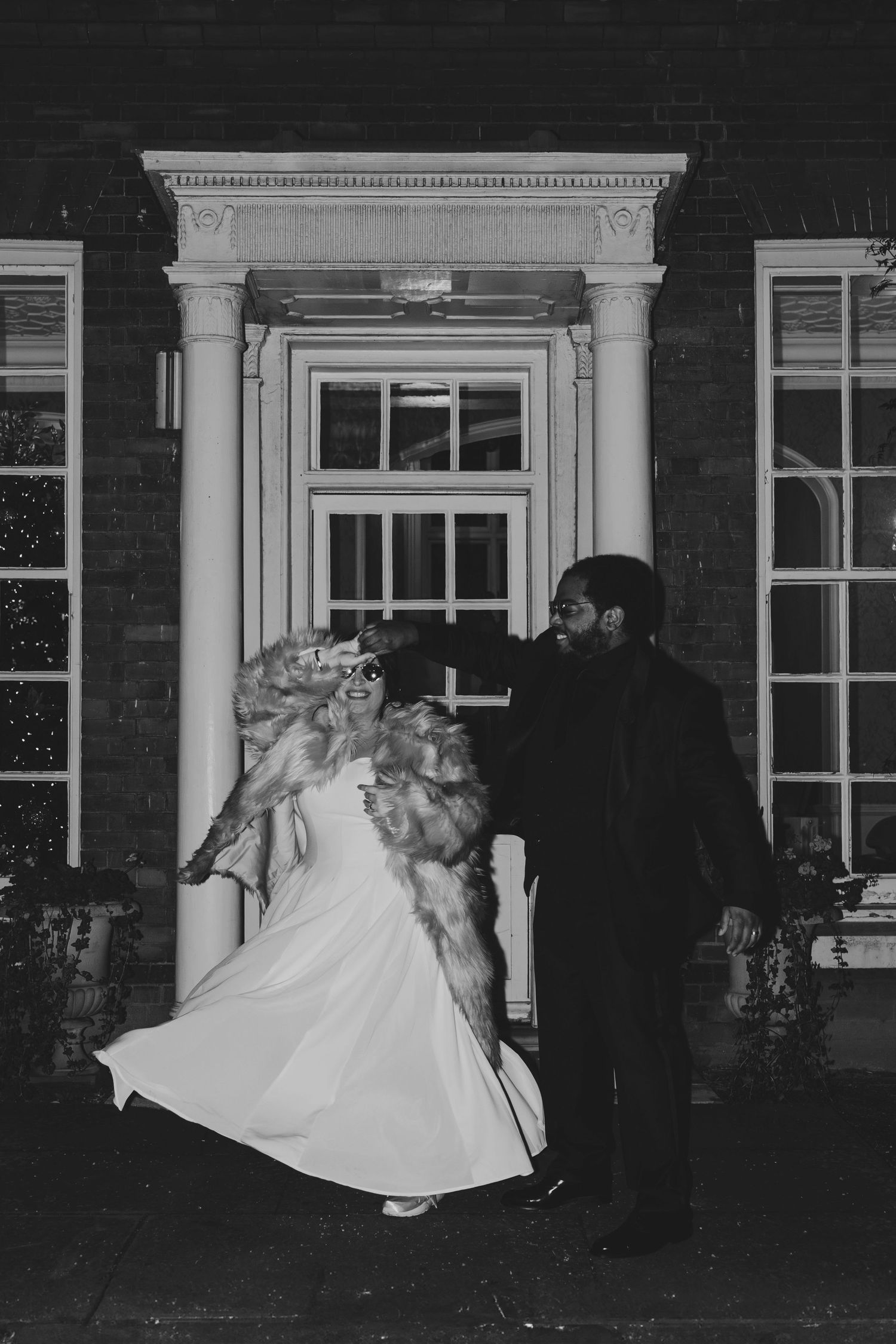Black and white photo of a bride and groom dancing outside an elegant brick building at night.