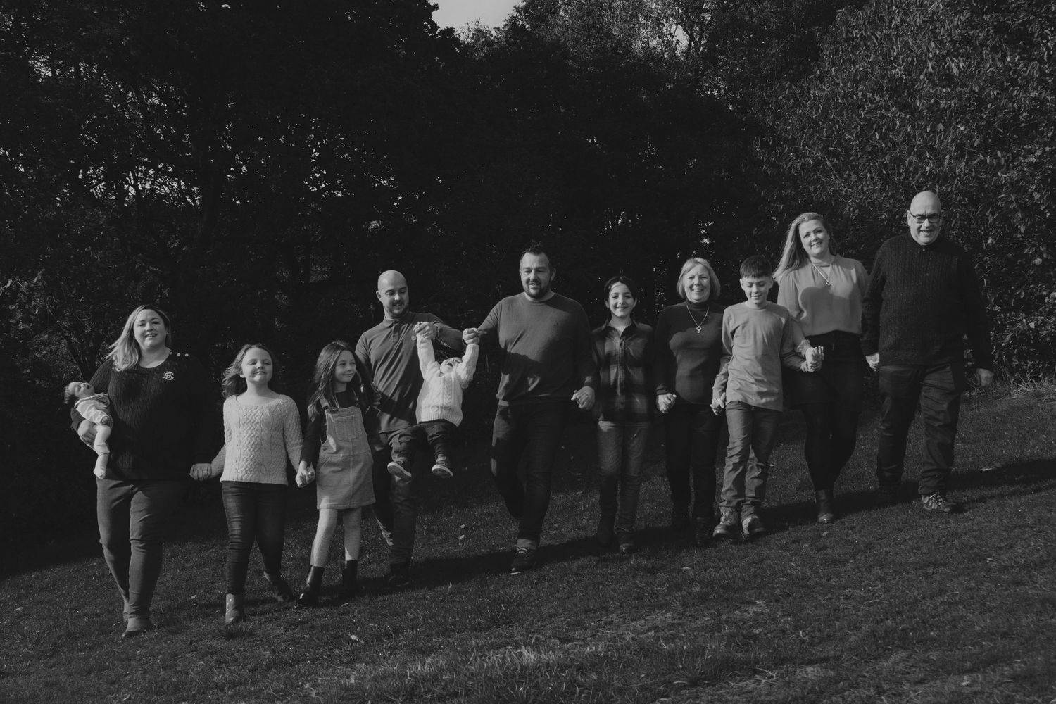 Black and white family portrait of large group walking together on grassy hill outdoors.