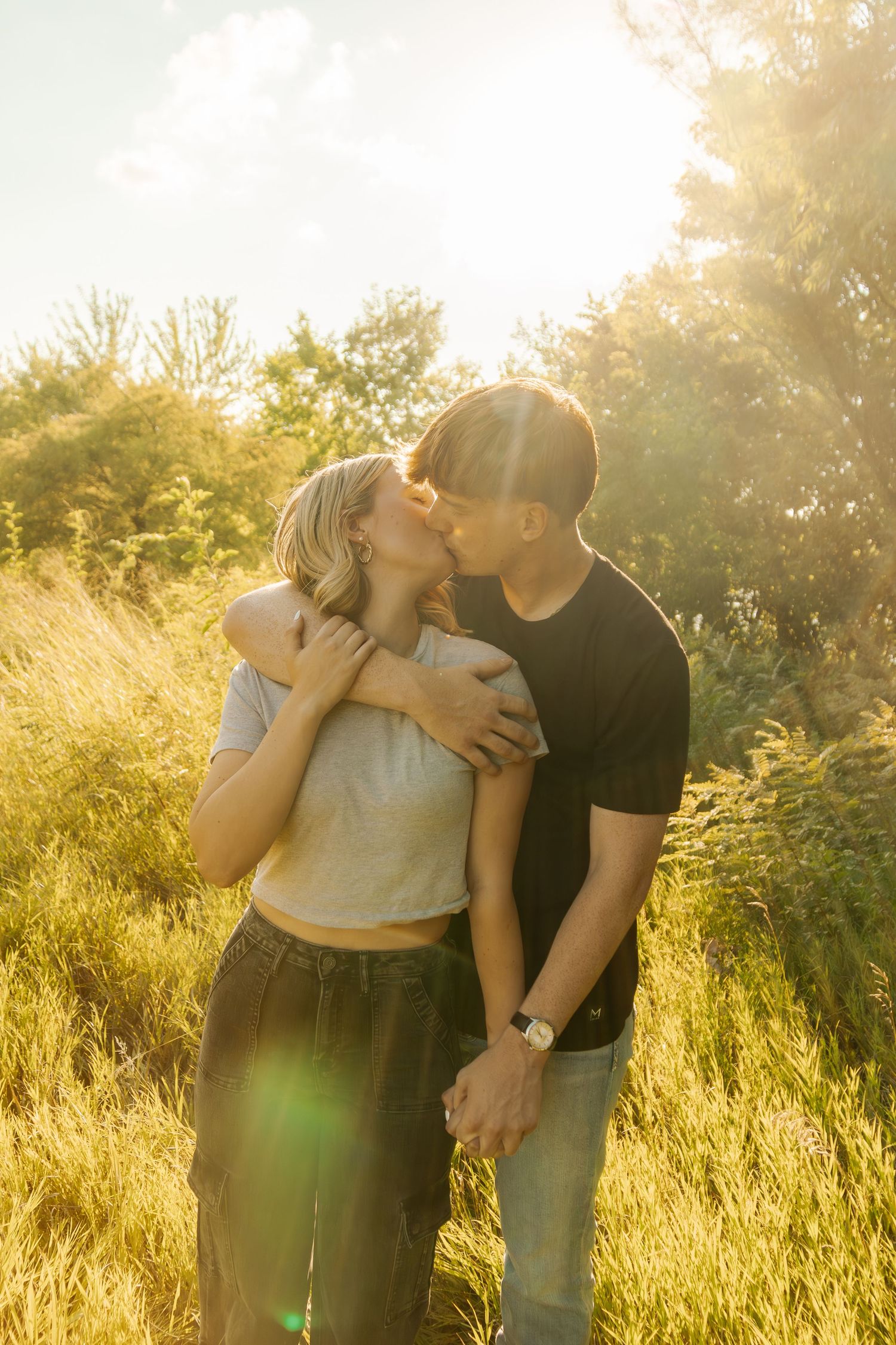 A romantic moment captured in a sunlit field with tall grass.