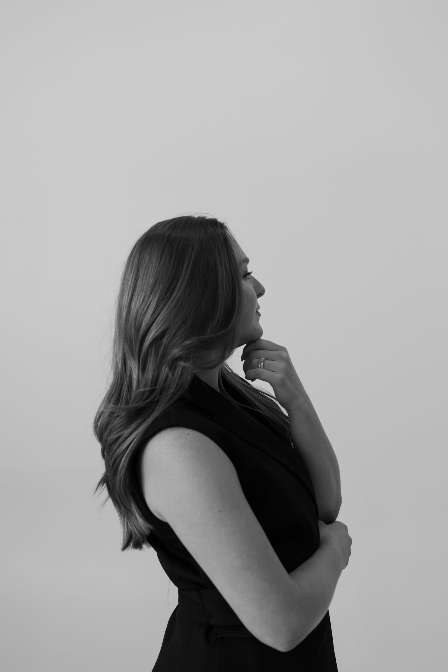 Side profile of person in black sleeveless dress against light background in monochrome.
