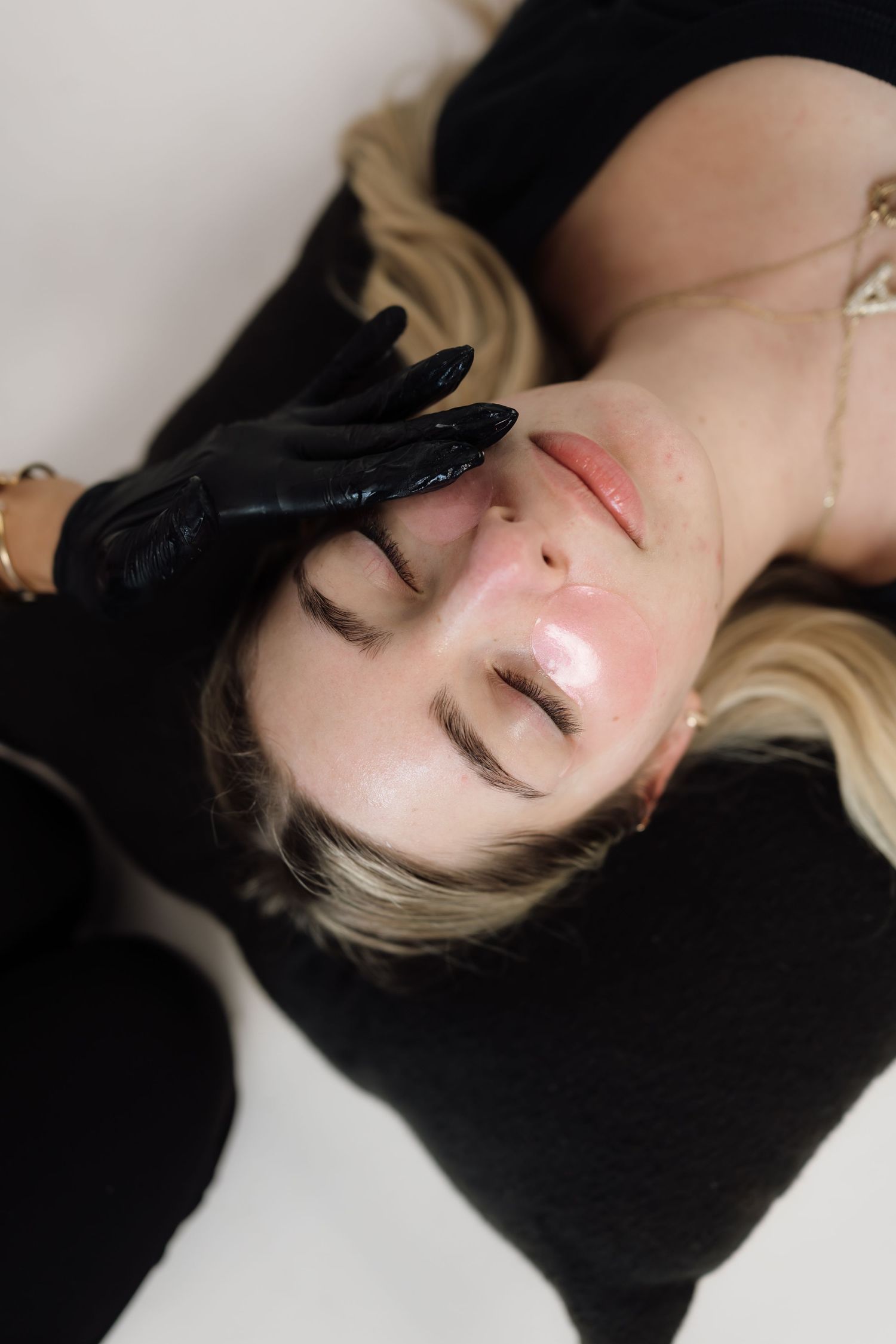 Side profile of beauty treatment with black gloved hands against white background.
