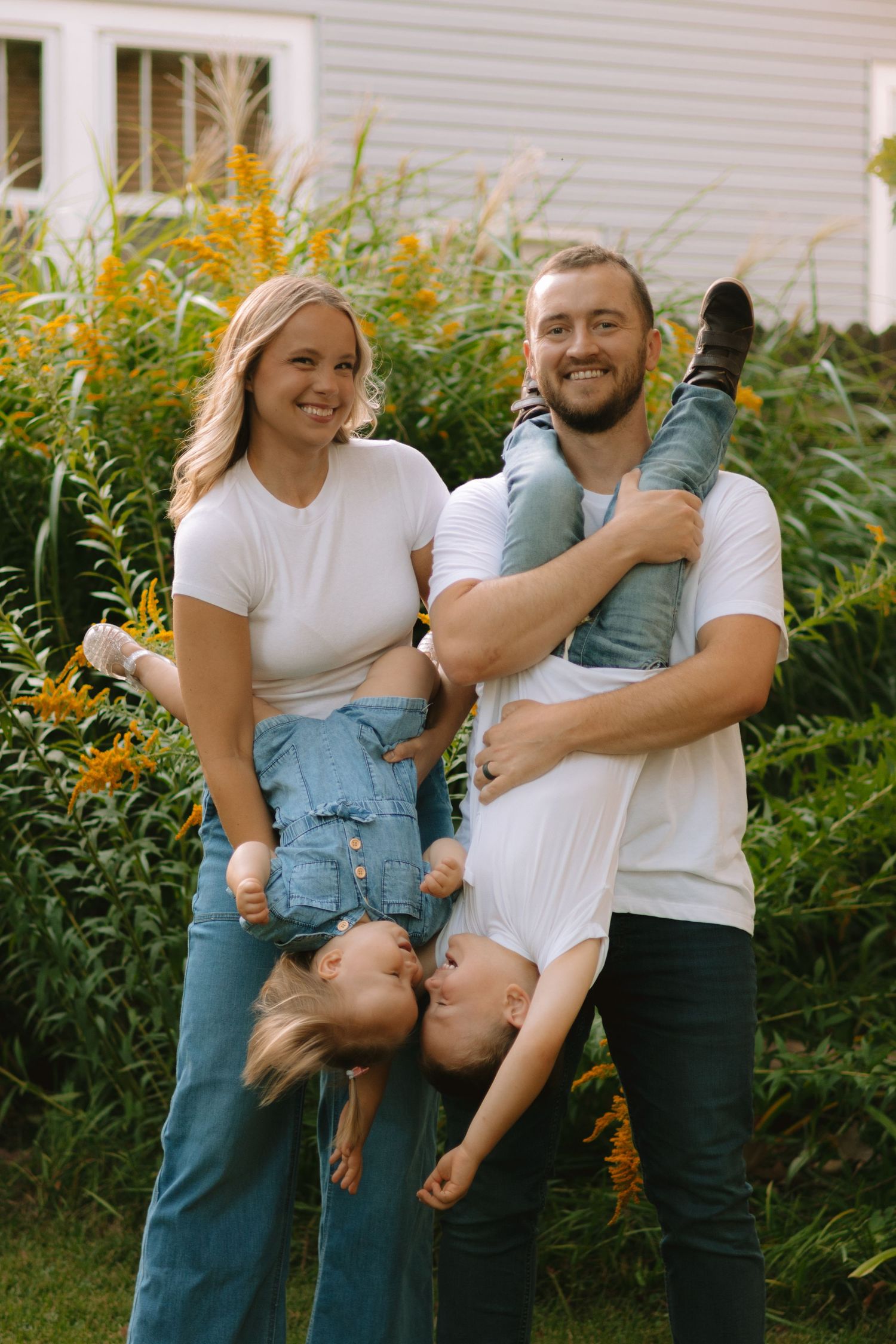 A family poses playfully in front of yellow flowers and a white house.