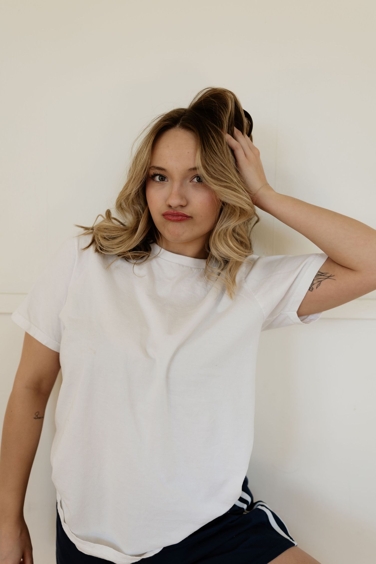 A series of four photos showing a person in a casual white t-shirt posing against a light-colored wall.