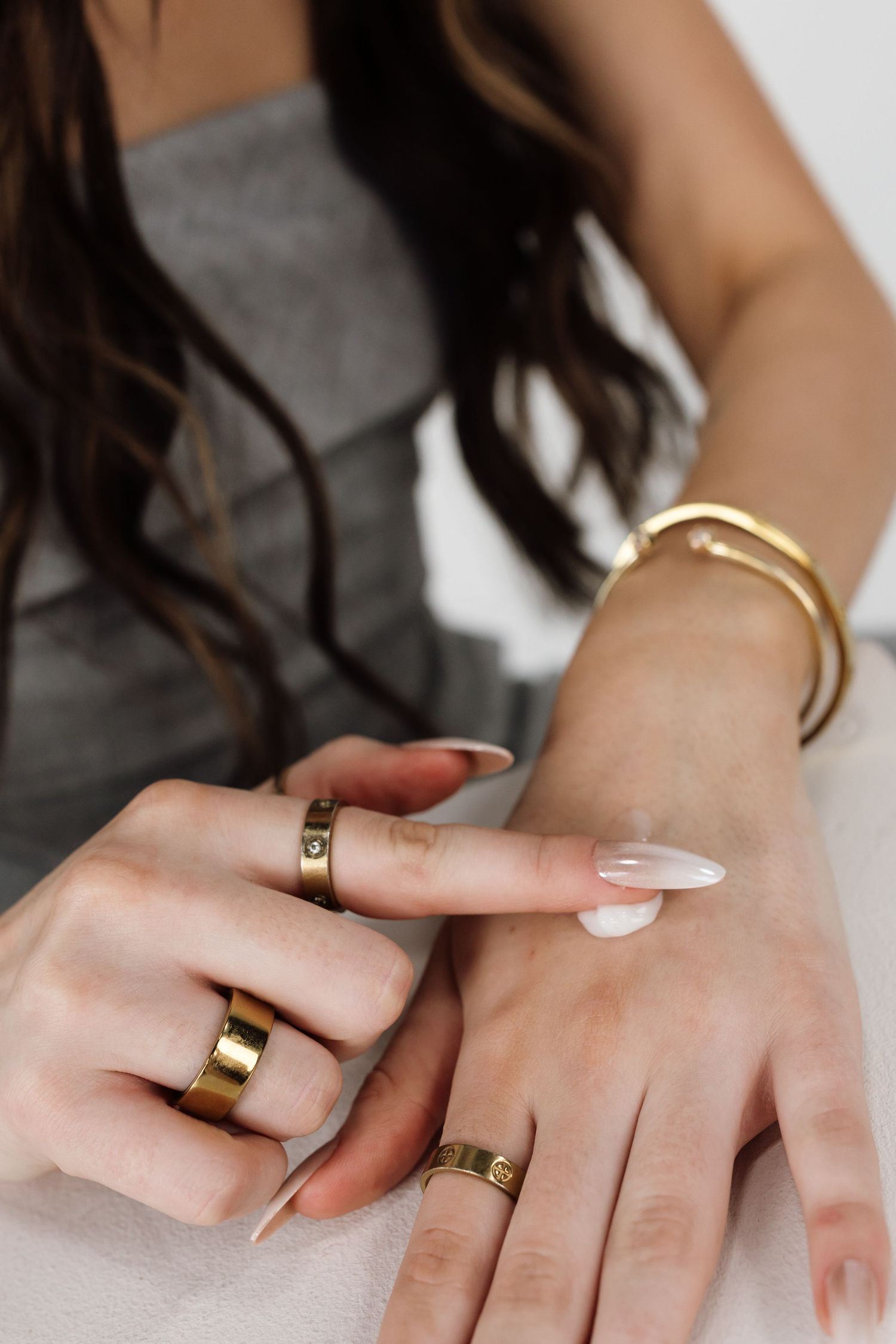 Detailed view of hands wearing gold rings and white nail polish against white background.