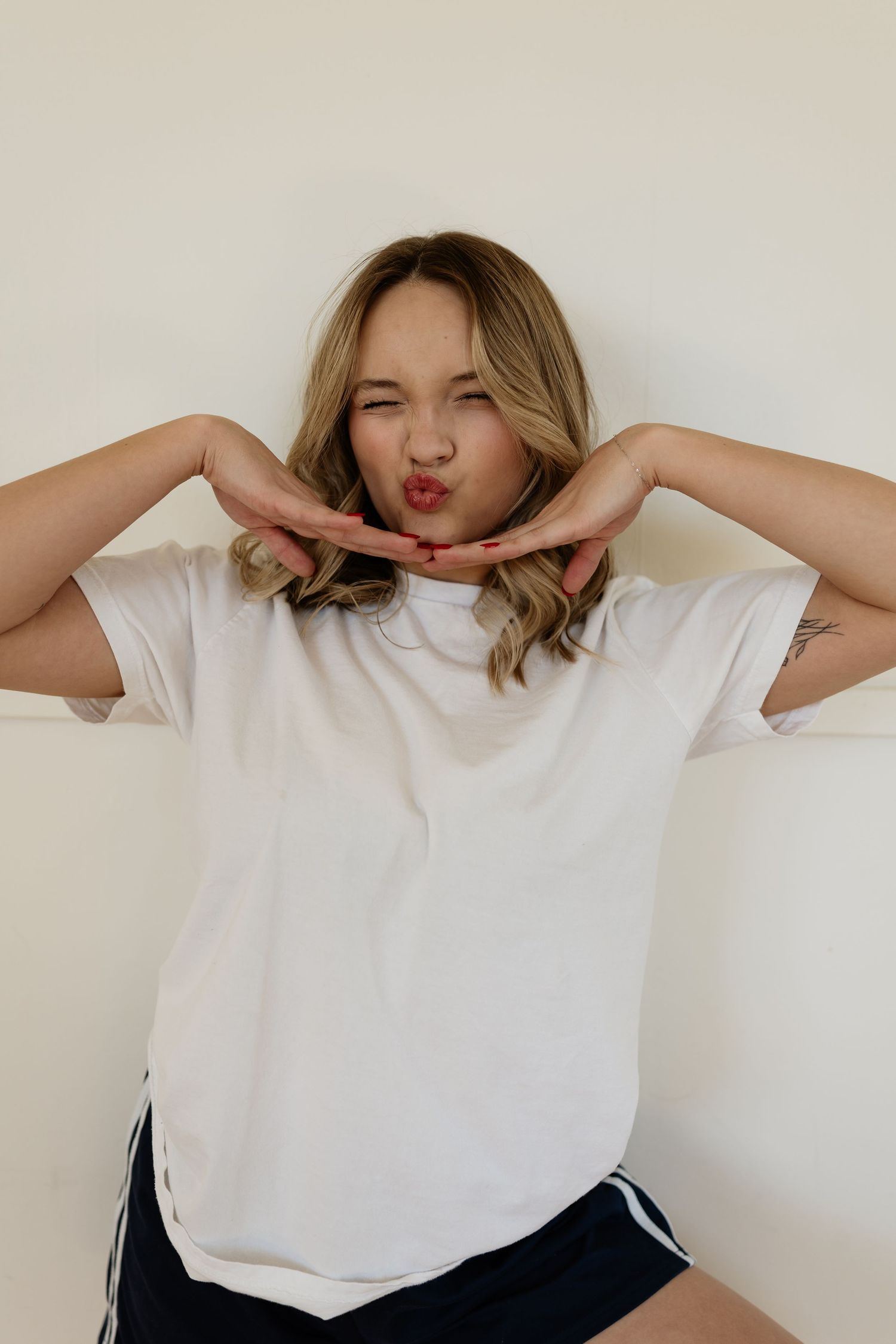 A series of four playful poses in a white t-shirt against a white wall showing different hand gestures and expressions.