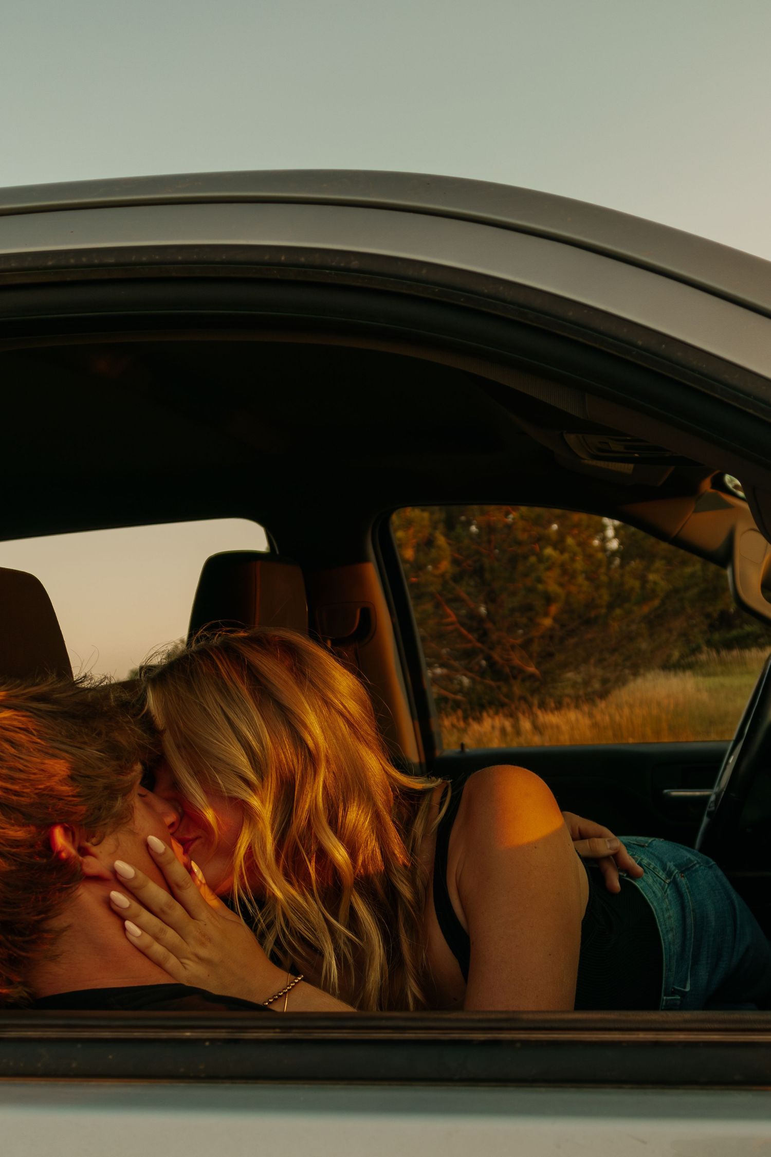 Two people embracing inside a car during sunset.