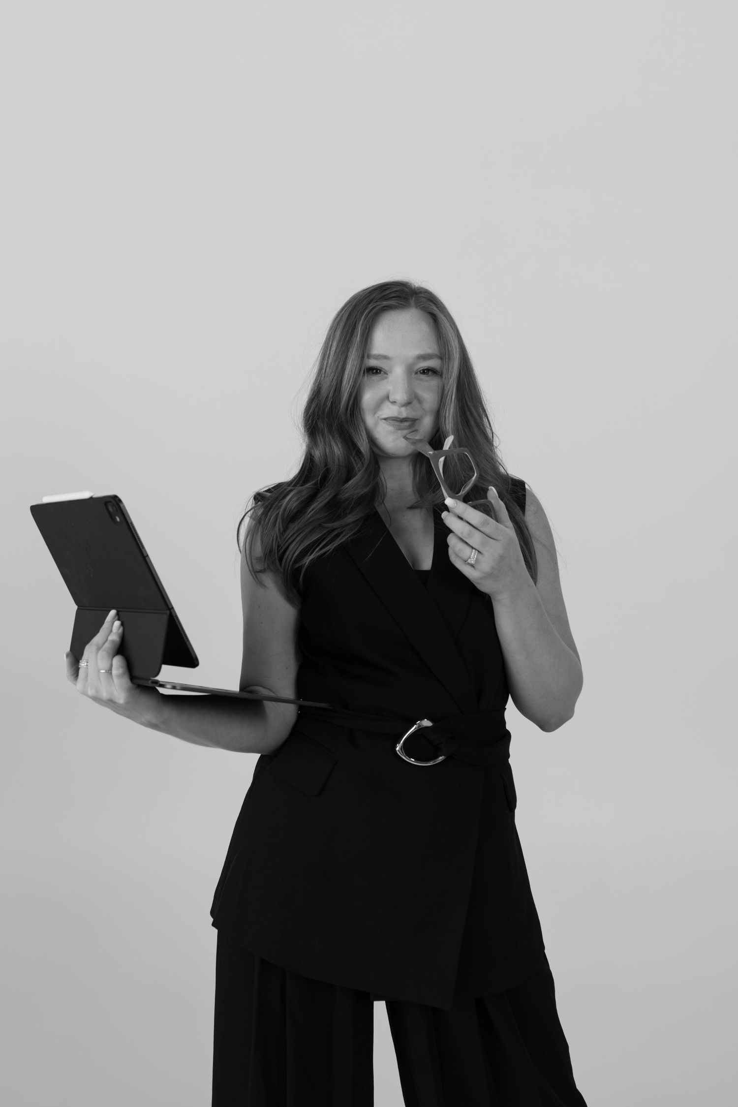 Person in sleek black outfit holds tablet while gesturing expressively.