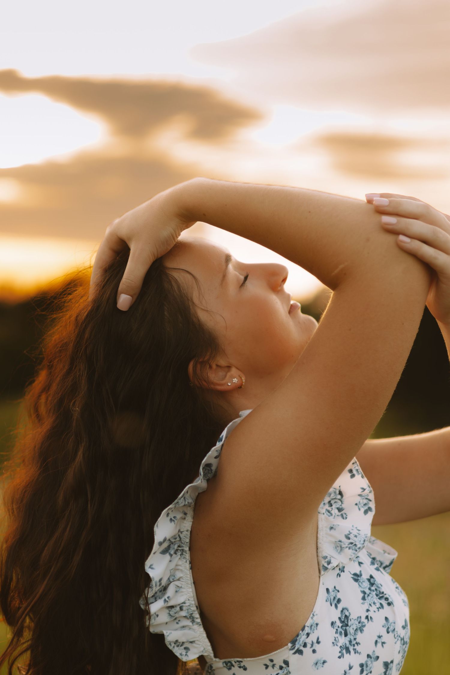 Artistic portrait against a sunset sky with delicate floral dress details and natural lighting.