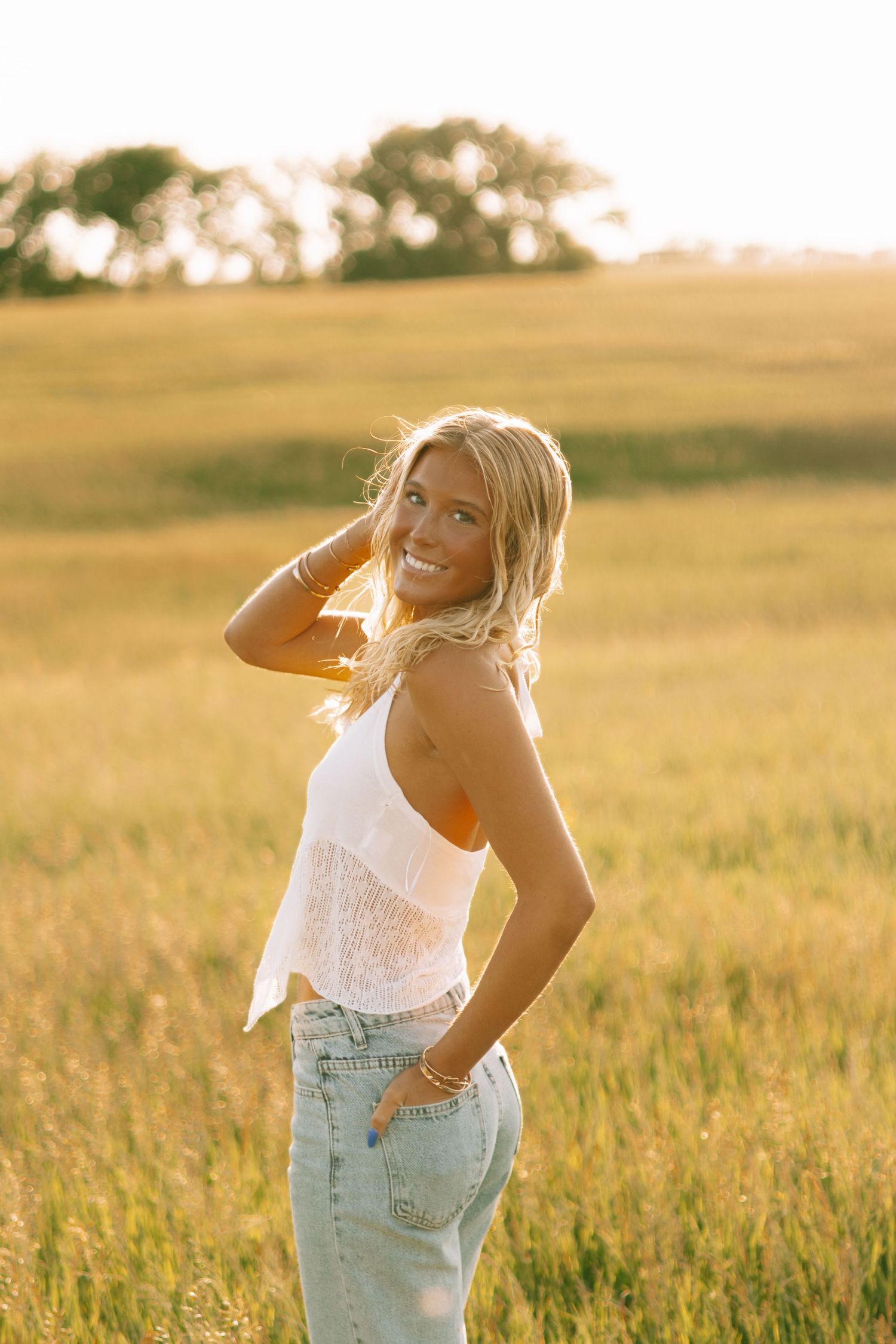 Carefree summer fashion shoot in a wheat field at sunset wearing denim and white top.