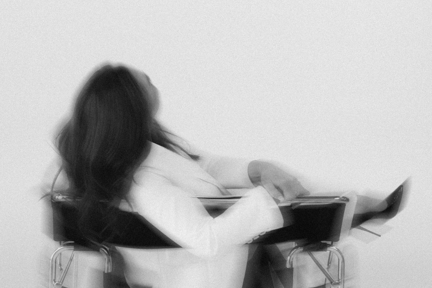 Artistic motion blur of a person in white clothing seated in a modern chair.